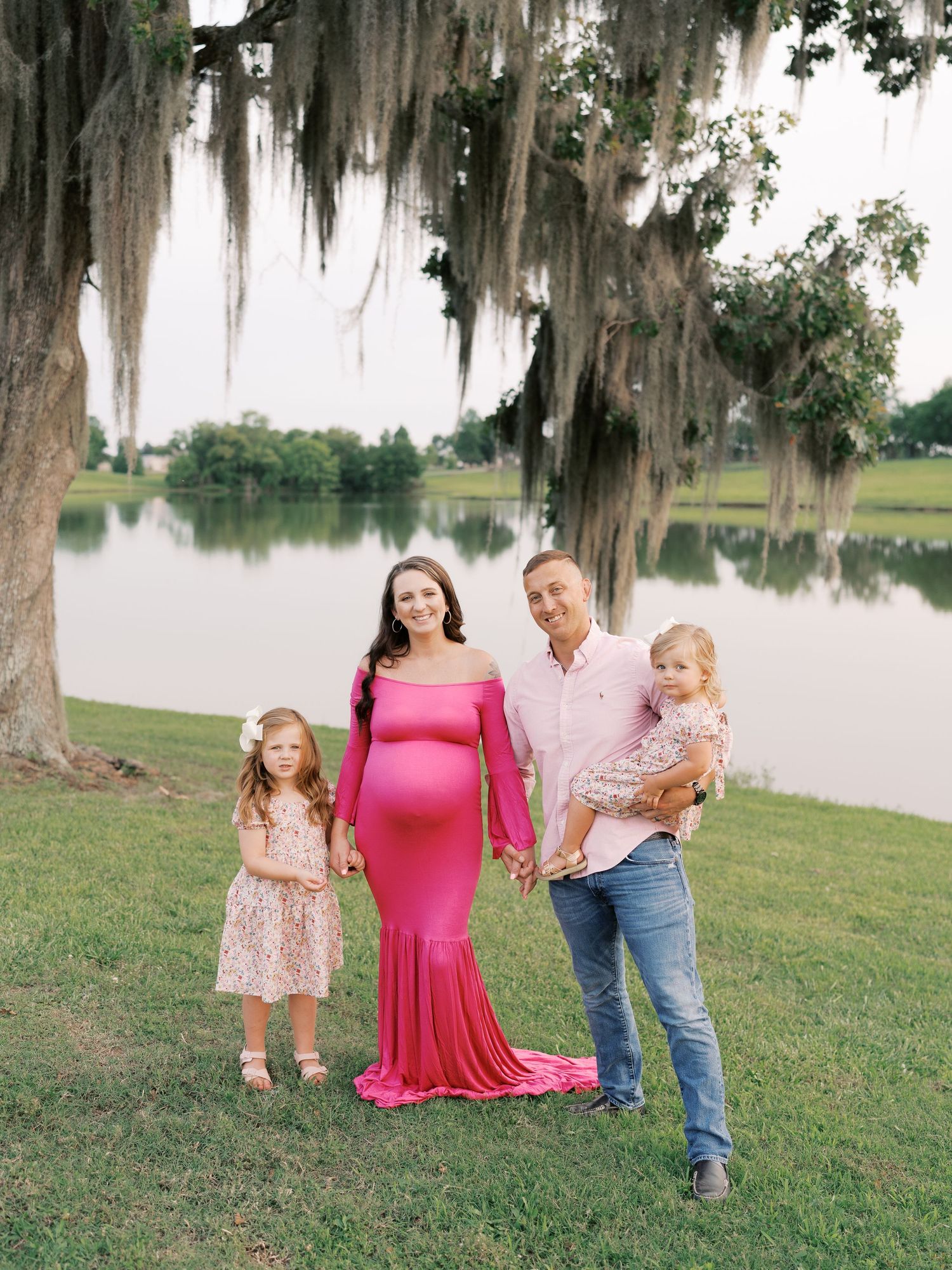 Family portrait under Spanish moss trees near a lake with coordinating pink and floral outfits.