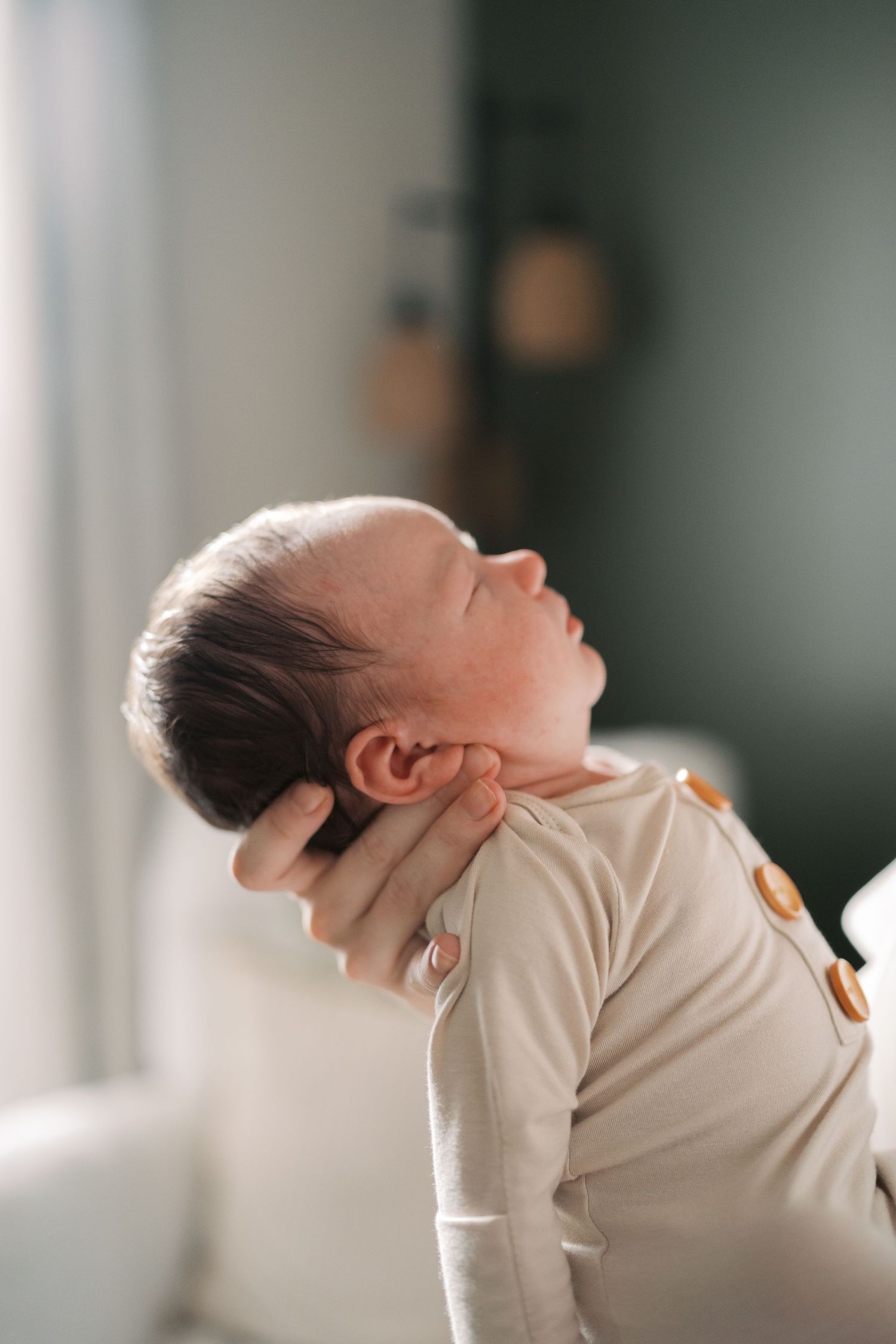 Close-up profile of sleeping newborn baby in beige onesie against dark background.