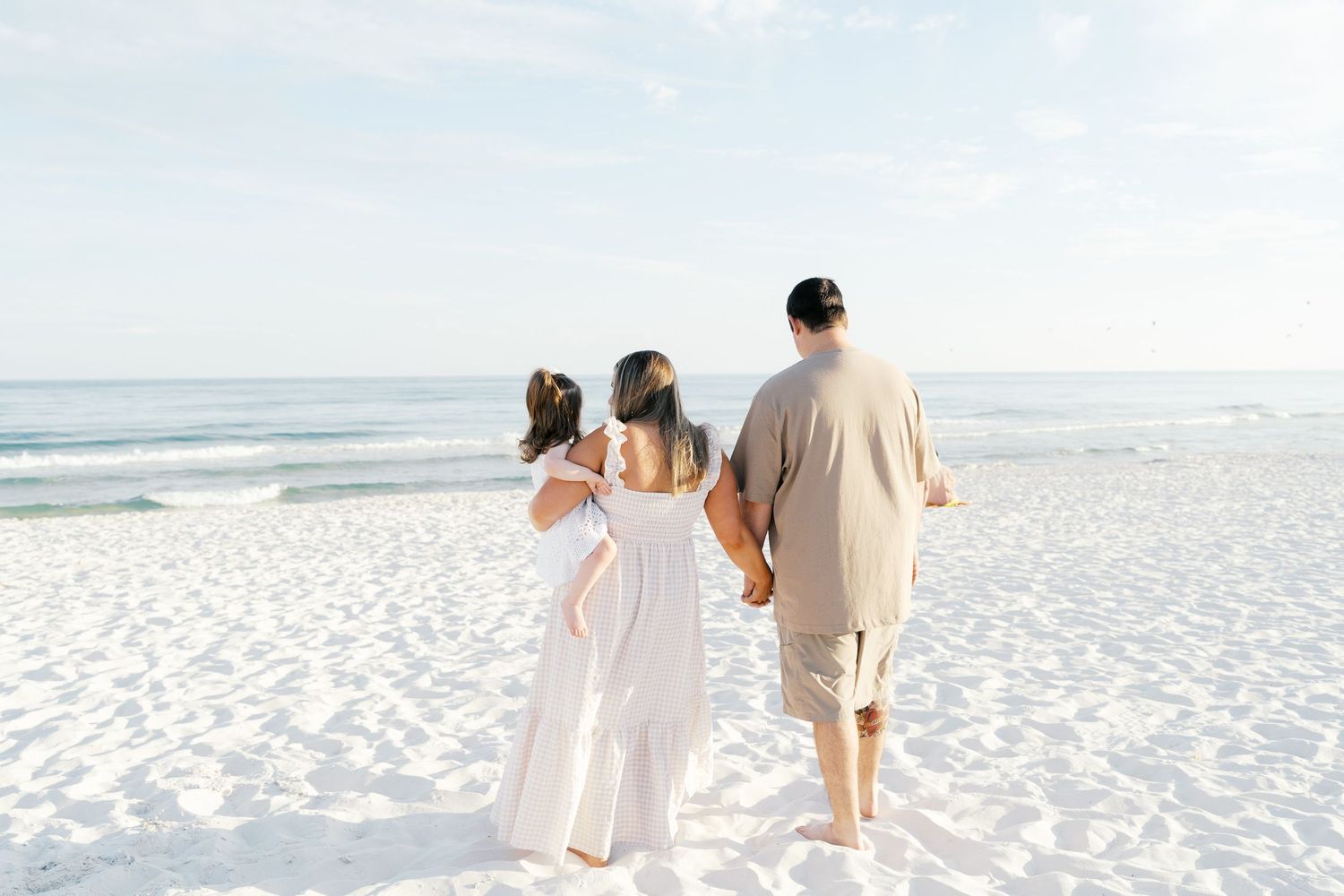 Family walking together on a pristine white sandy beach at sunset with ocean waves in the background.