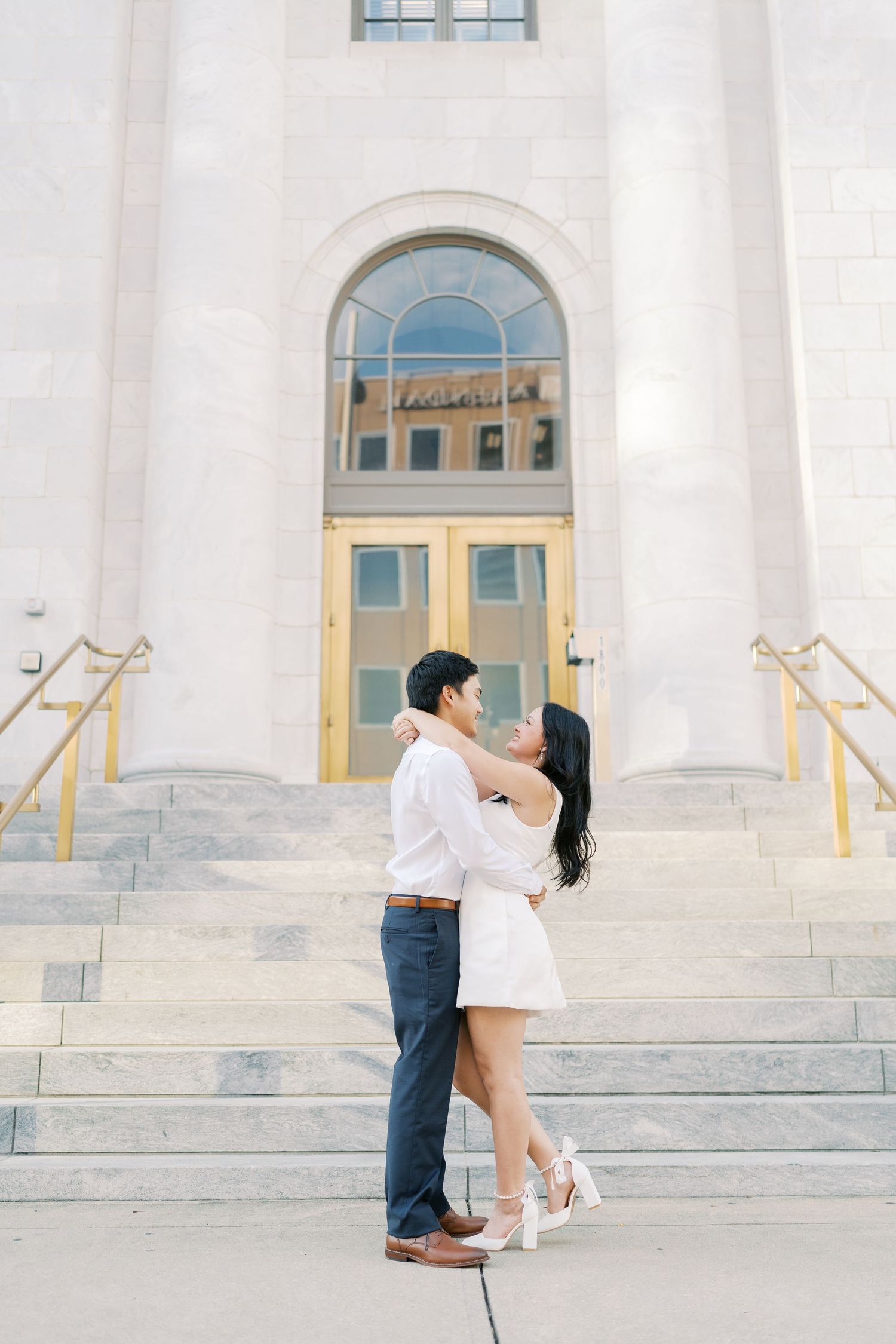 Couple embracing on grand white stone steps of a neoclassical building.