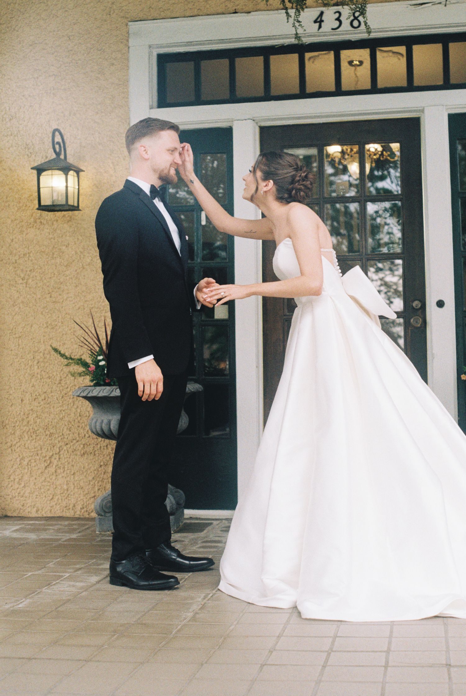Wedding couple interaction on a white tiled porch outside a residential entrance.