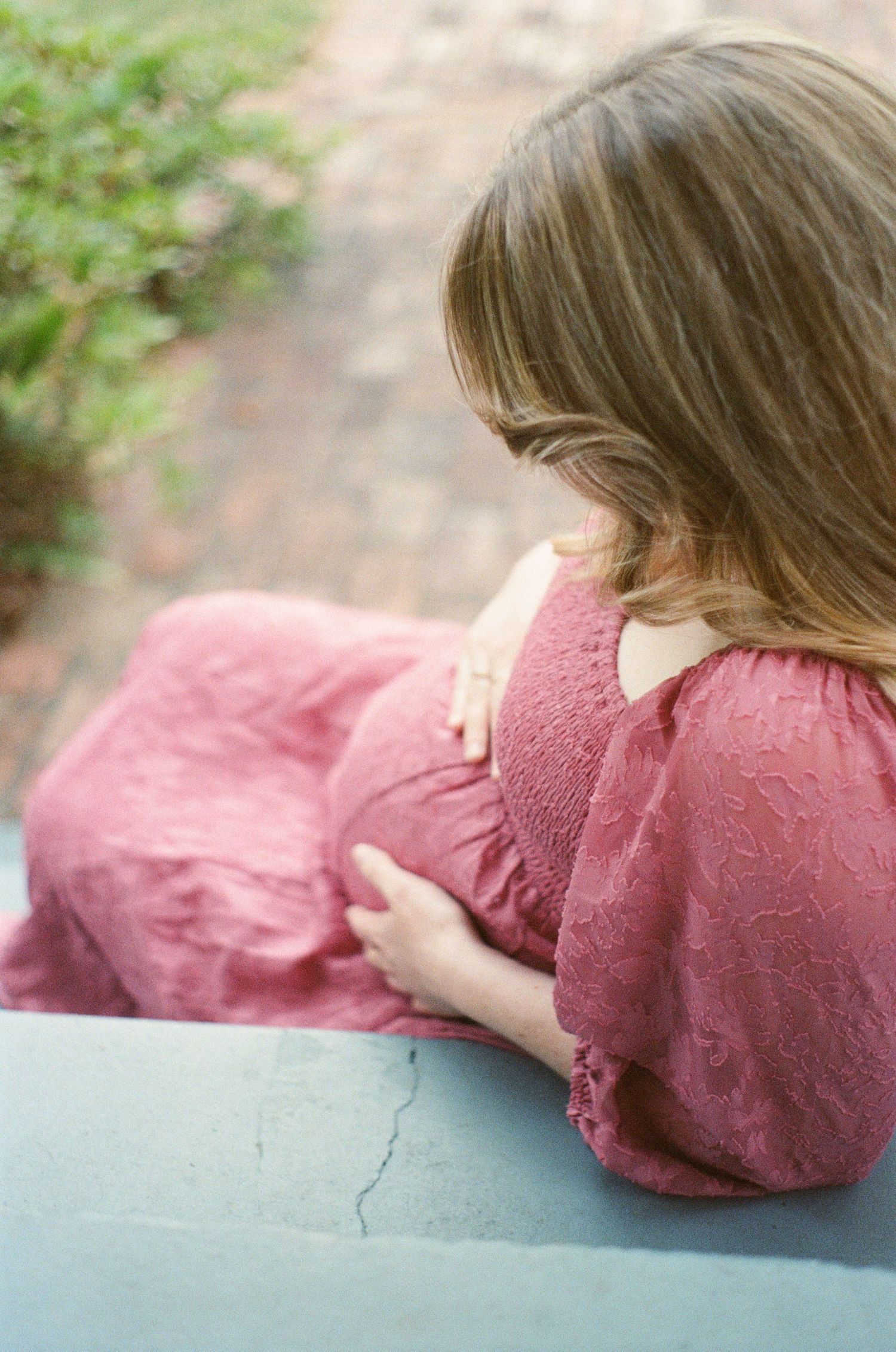 Person in pink sweater lying on blue surface in artistic portrait composition.