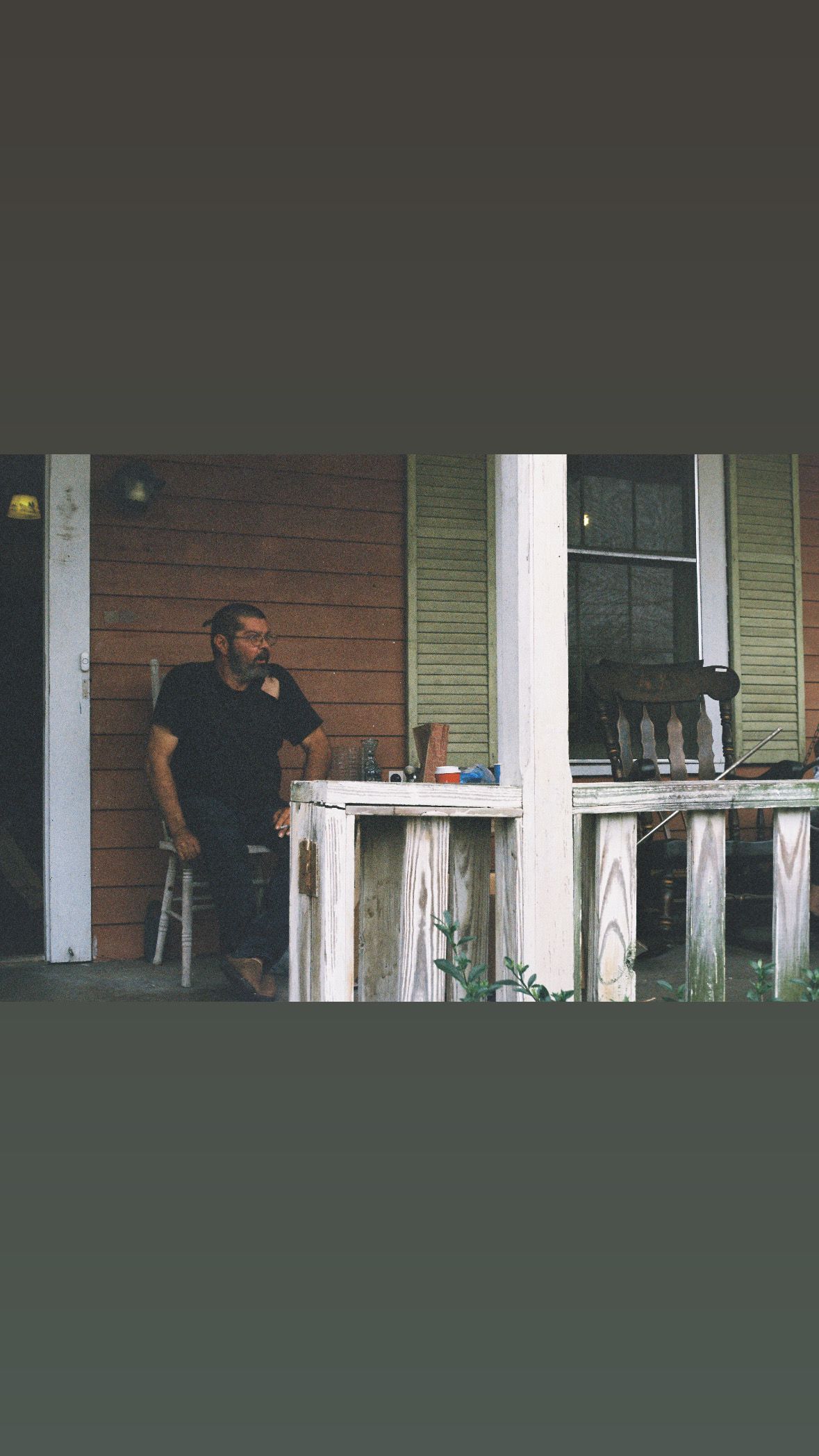 Man standing on a rustic front porch of a house with white columns.