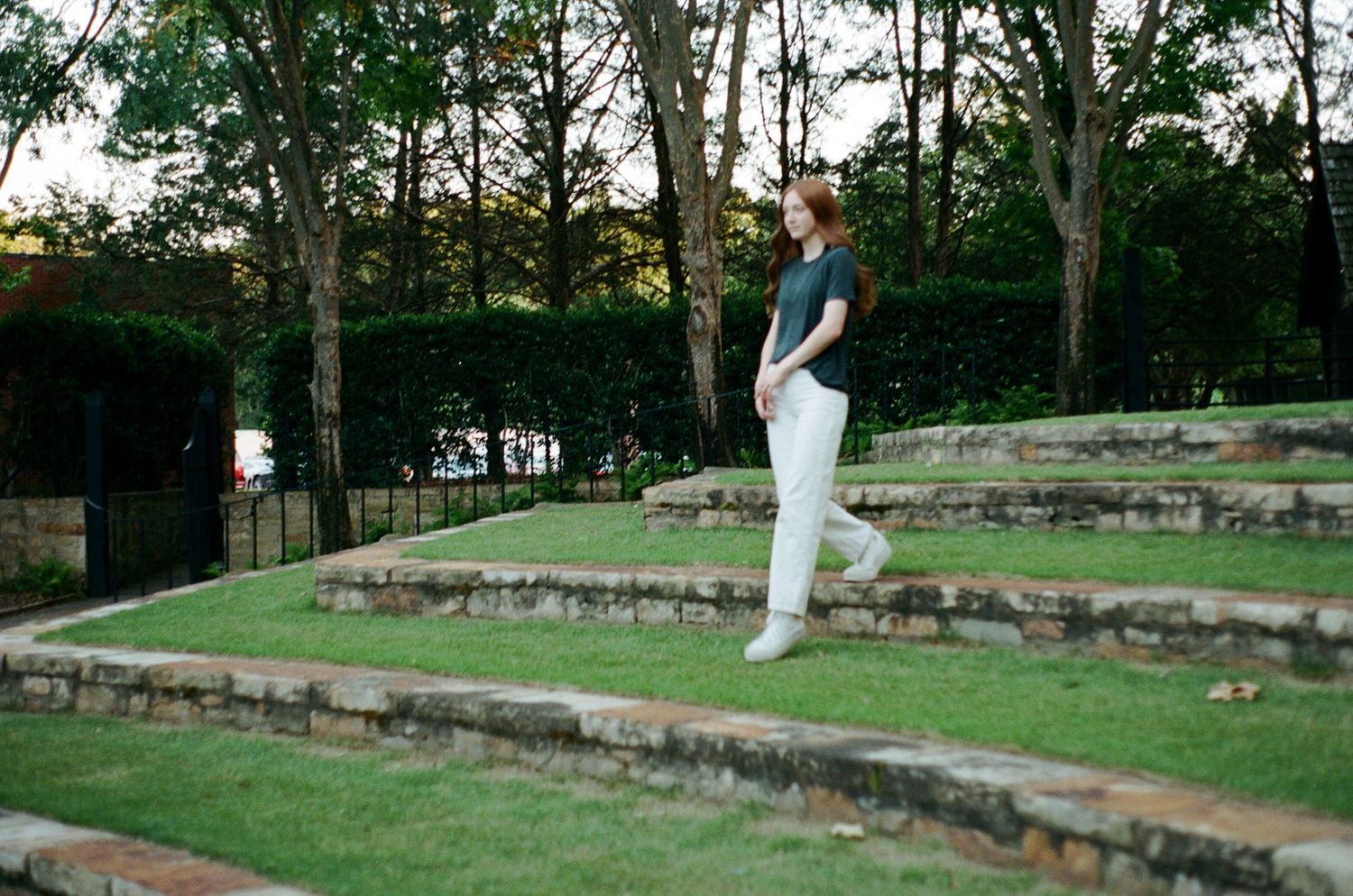 Figure standing on tiered garden steps surrounded by trees at dusk.