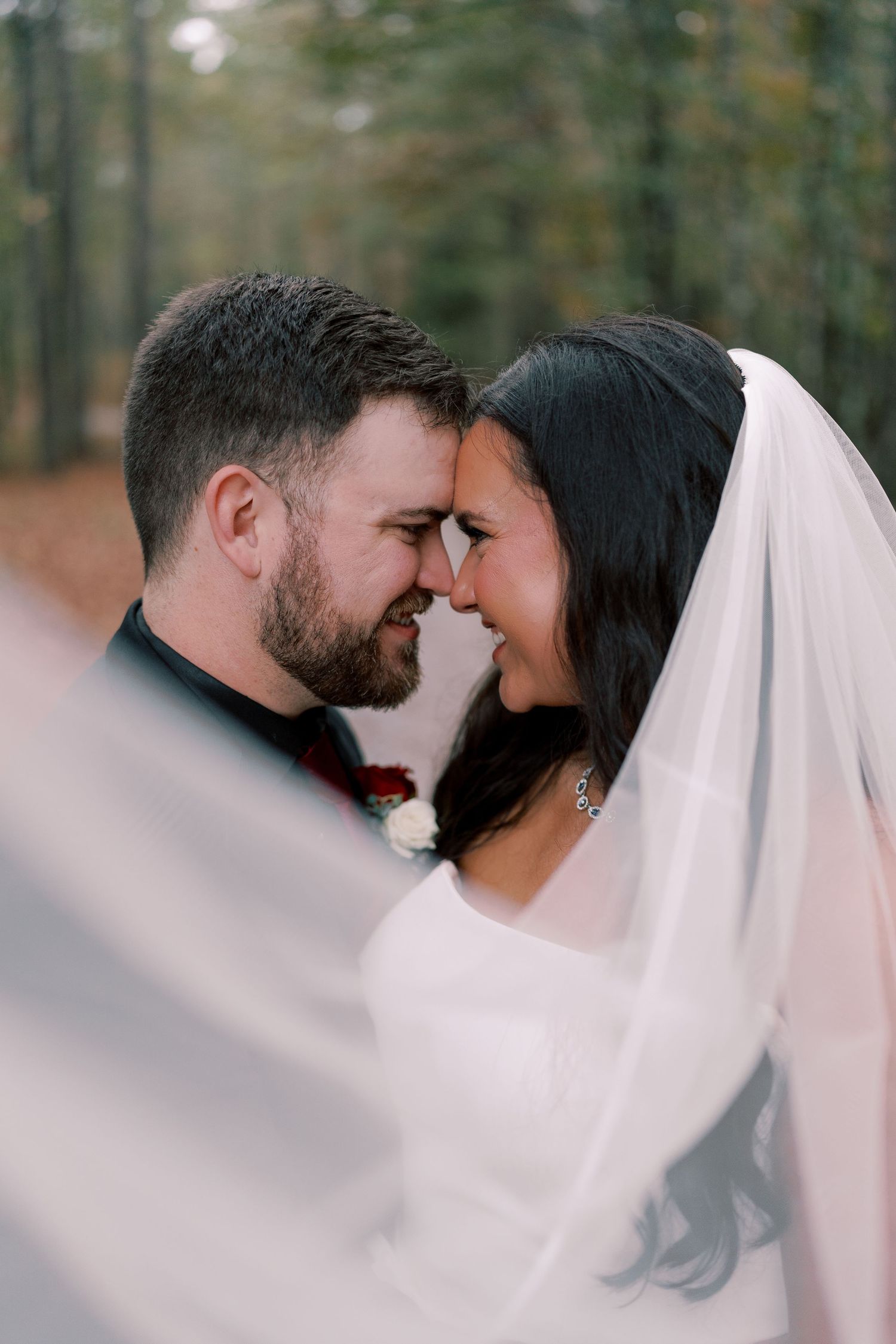Romantic wedding portraits in soft focus with flowing white veil against forest backdrop.