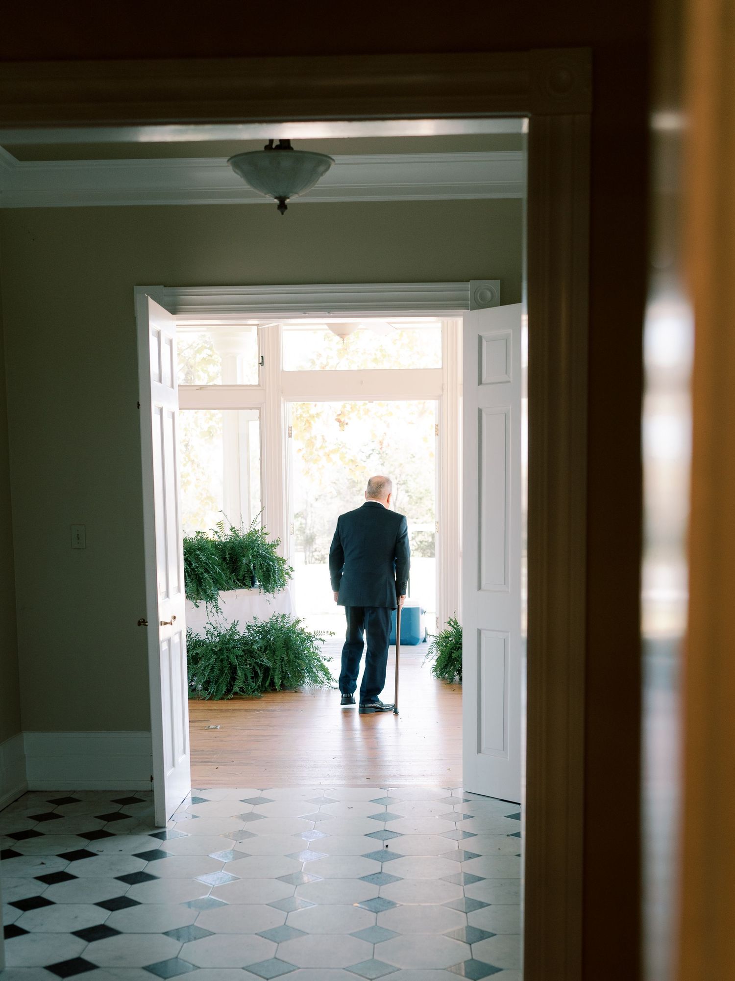 Silhouette through doorway standing in sunlit entryway with checkered floor.