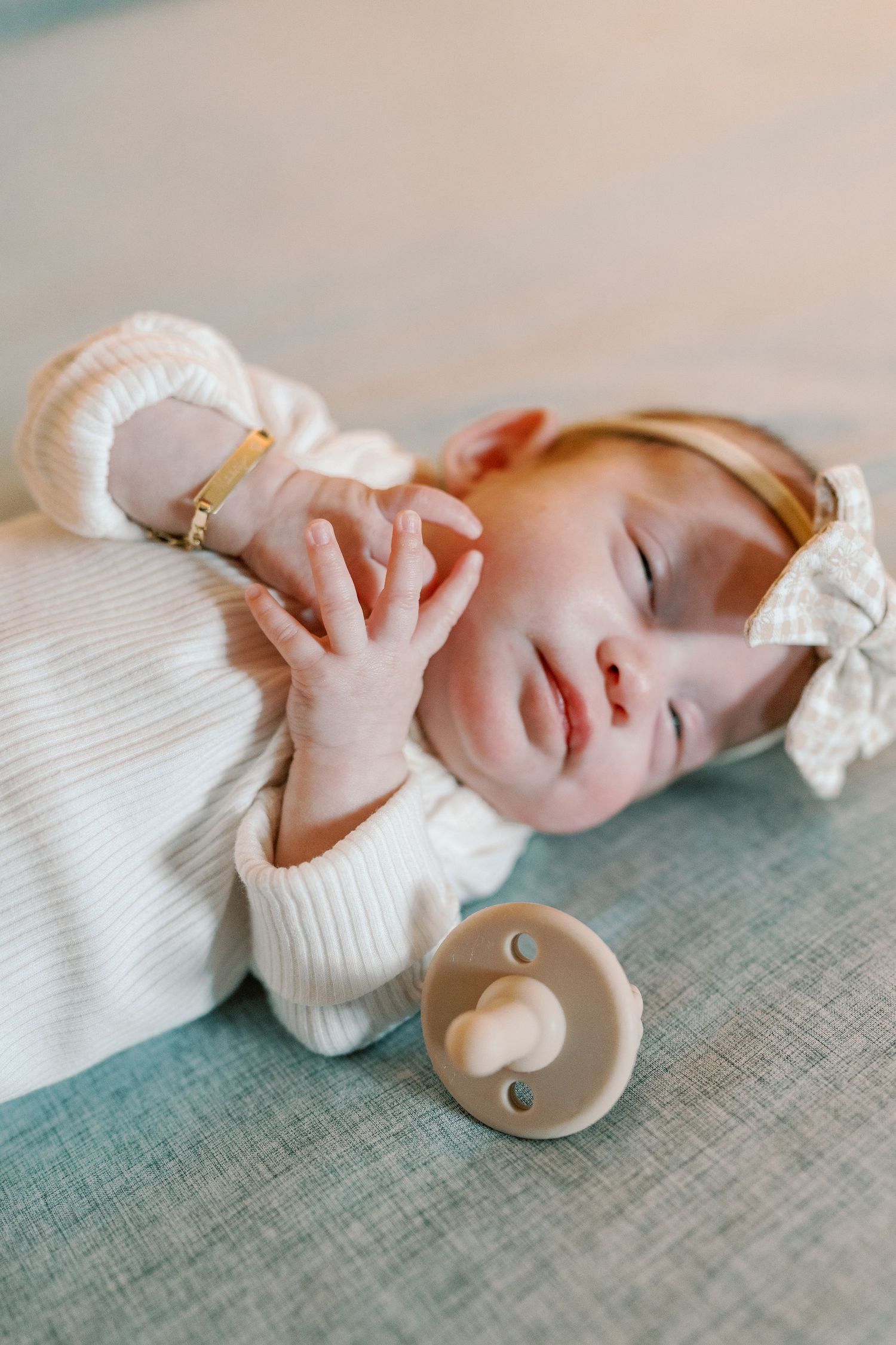 Newborn baby sleeping peacefully on textured fabric with a wooden teething toy.