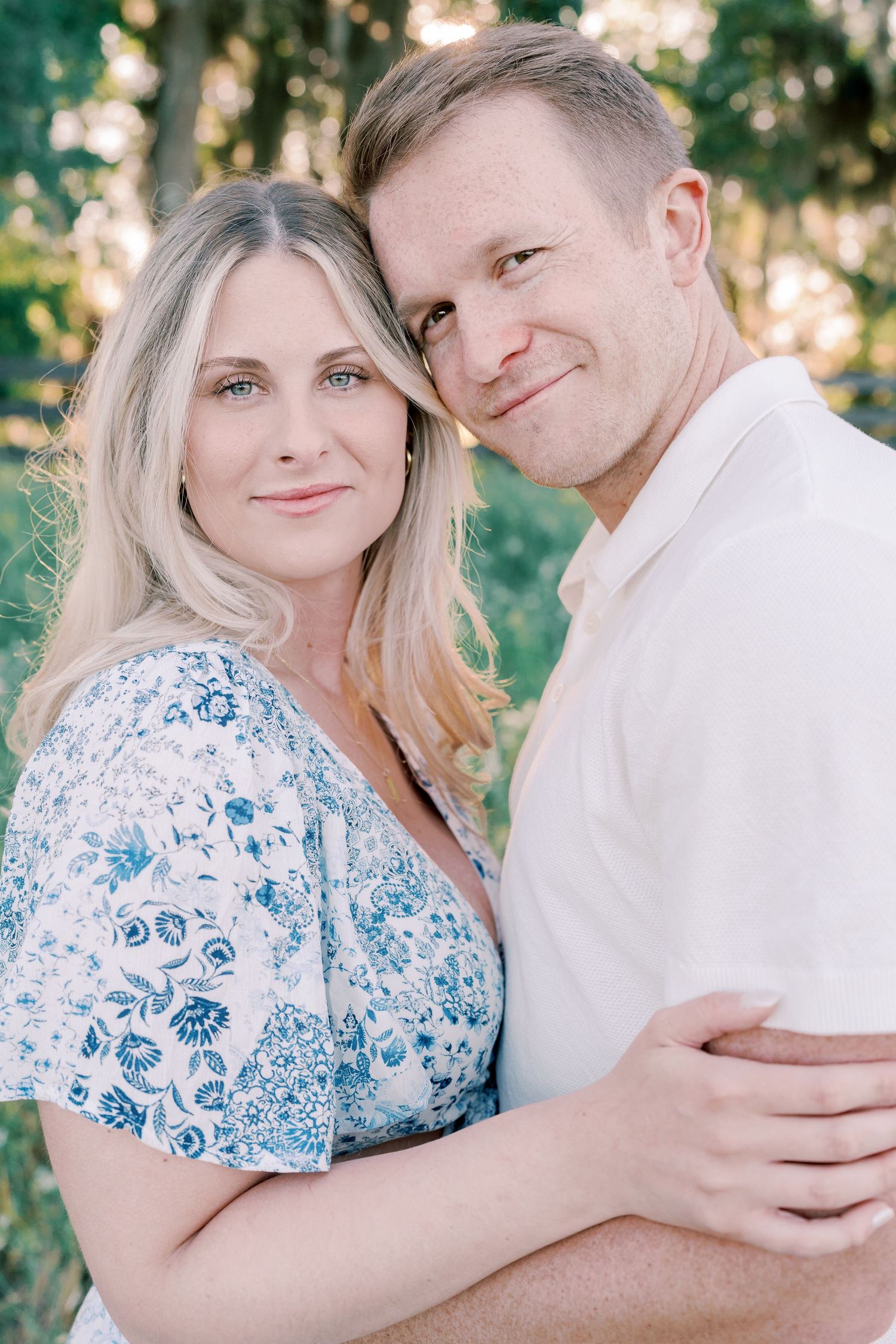 Sweet outdoor portraits of couple in white shirt and blue floral dress against green background.