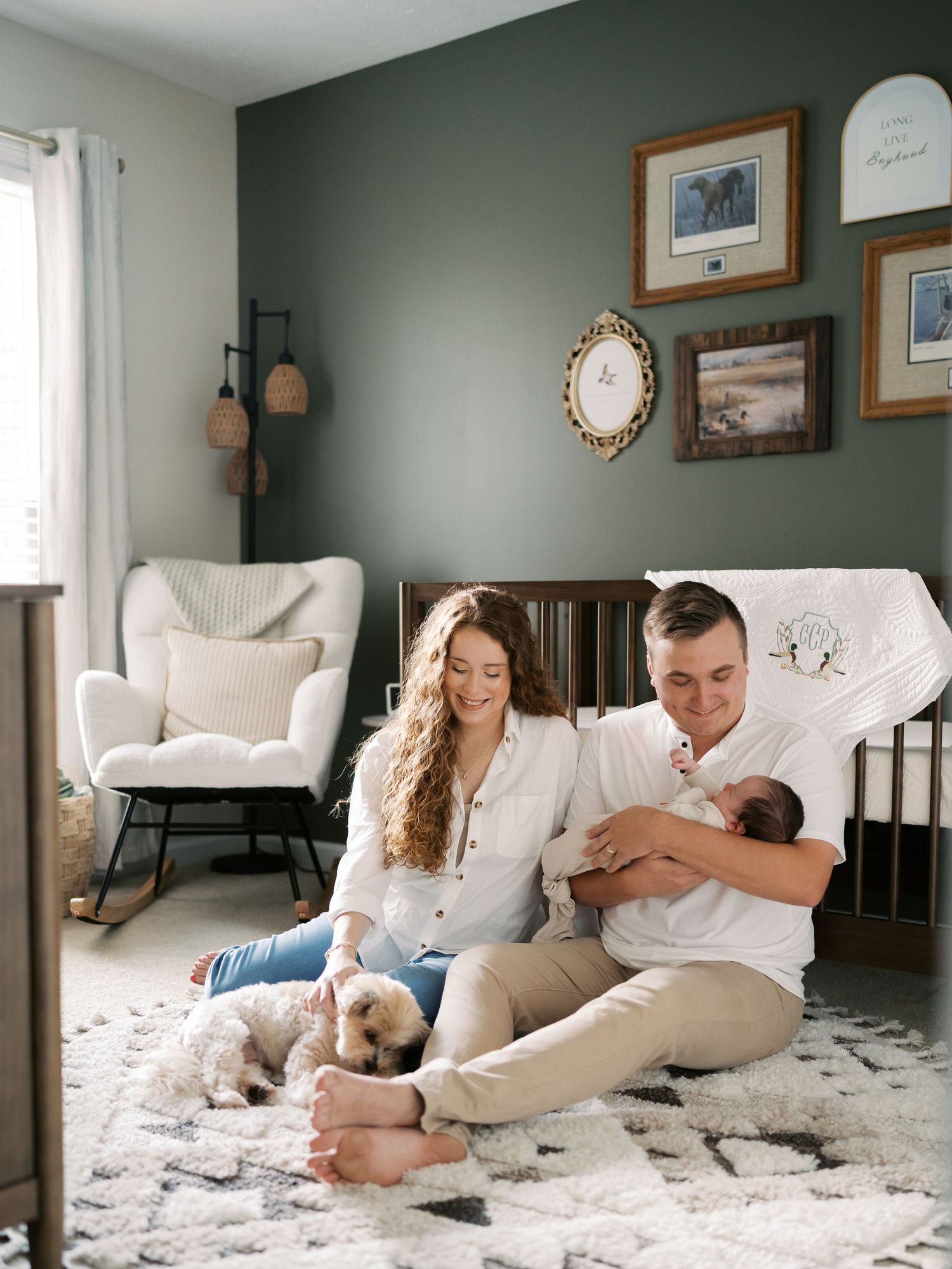 Family and pet dog share loving moments together on white rug in contemporary nursery space.