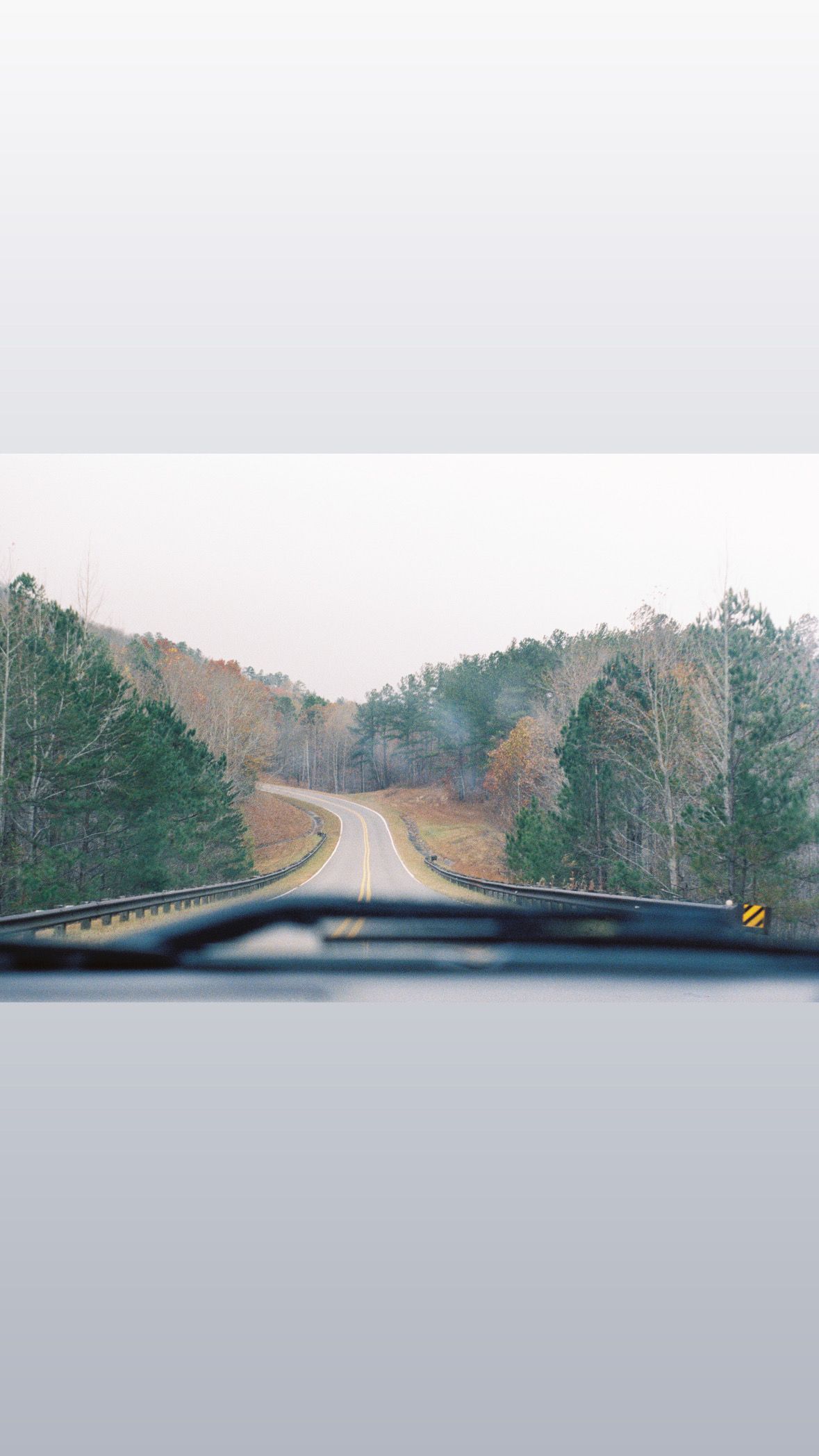 View of a winding rural road through car windshield on a cloudy day.