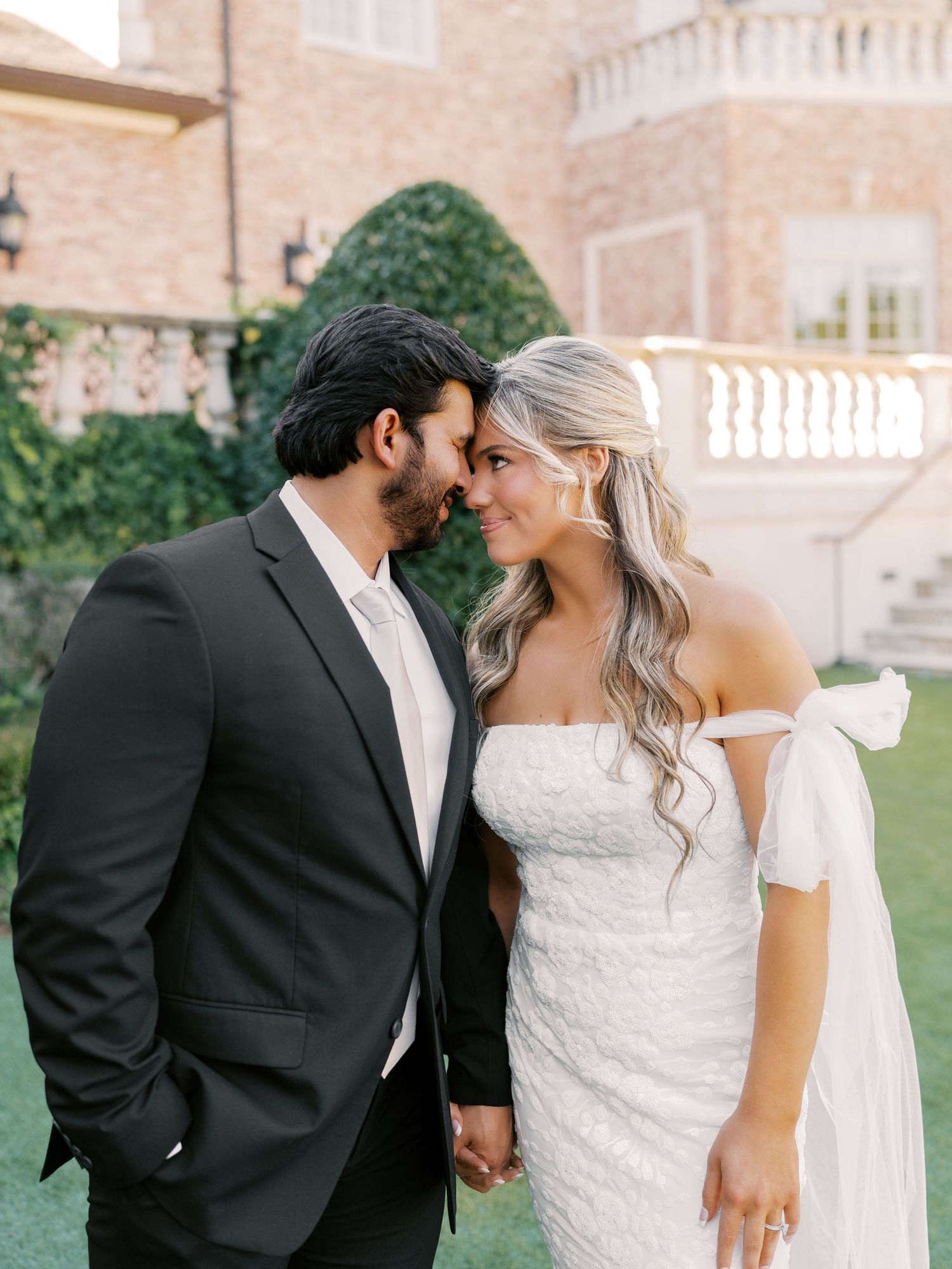 A tender moment shared between newlyweds outside an elegant brick mansion.