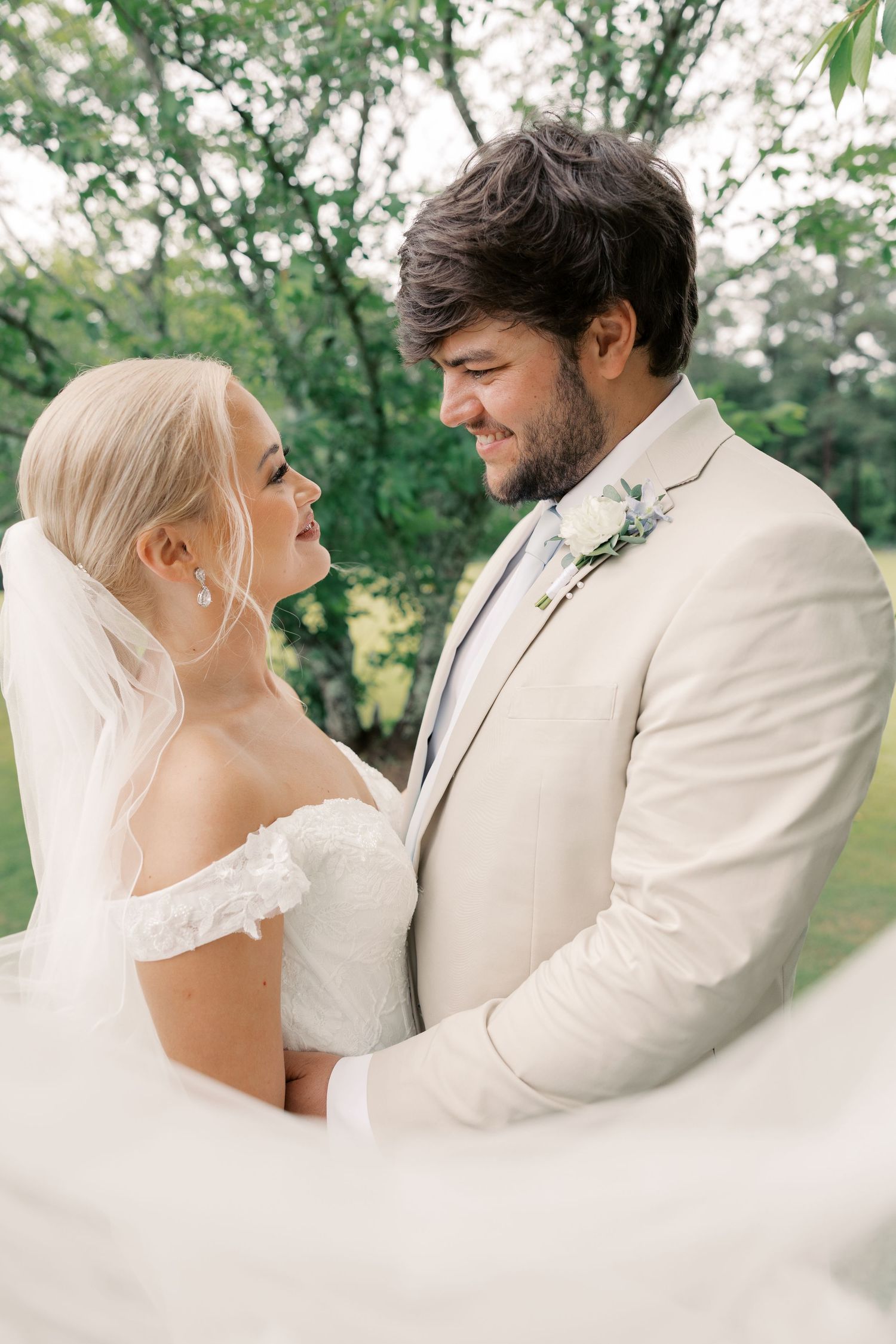 Romantic wedding couple in white attire embracing outdoors in a garden setting.