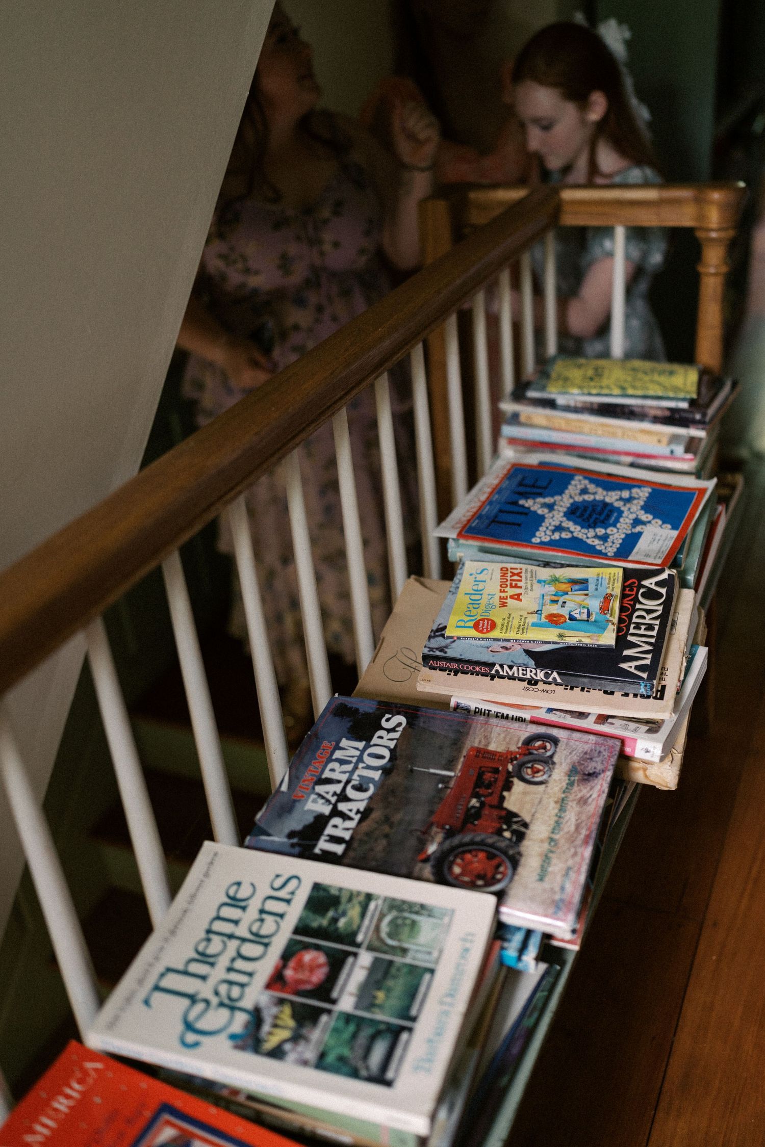 Collection of books stacked along wooden staircase railing.