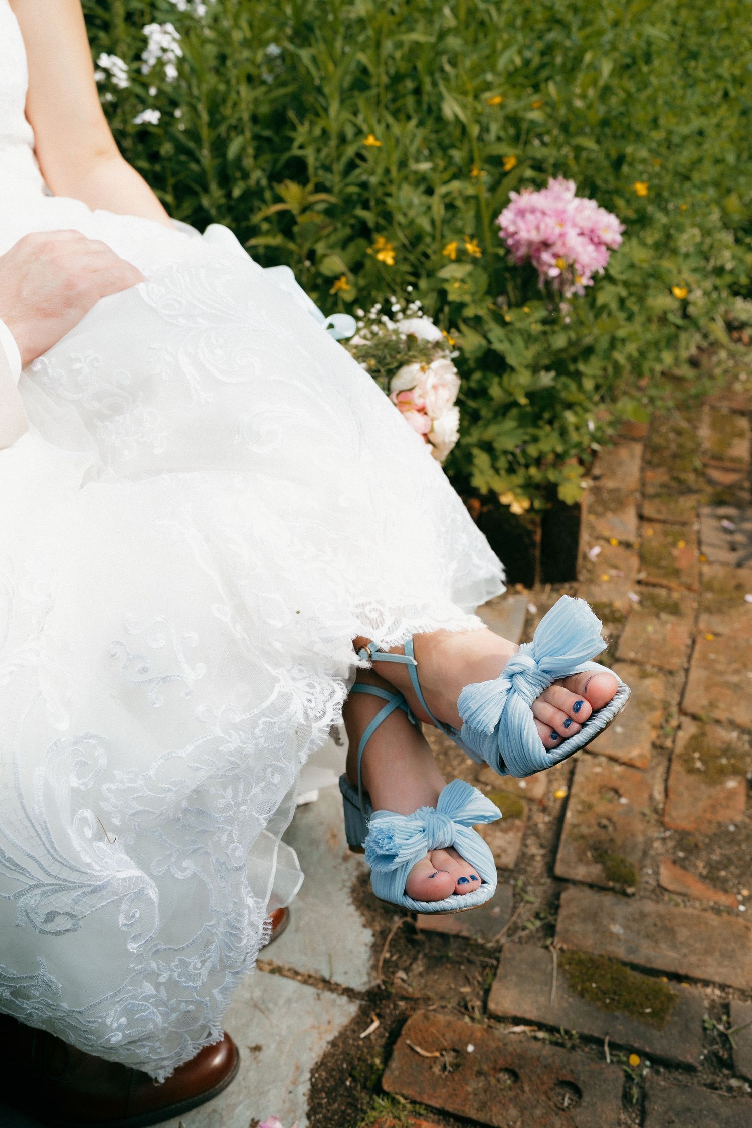 Close-up of bride's feet in blue bow sandals peeking out from under white wedding dress.