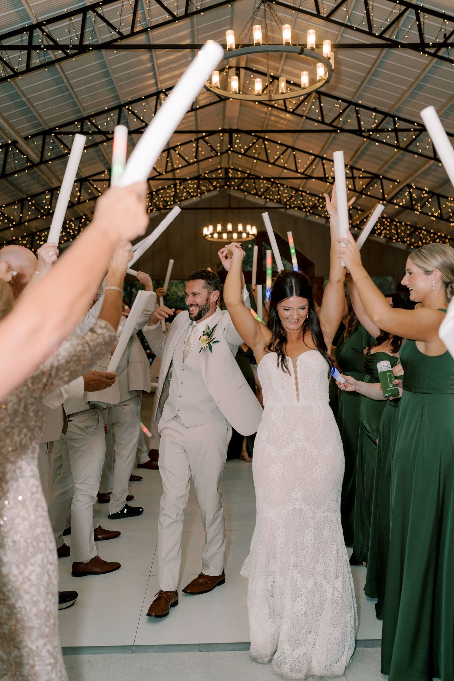 Wedding reception dance party with guests in formal attire holding light sticks under industrial ceiling.
