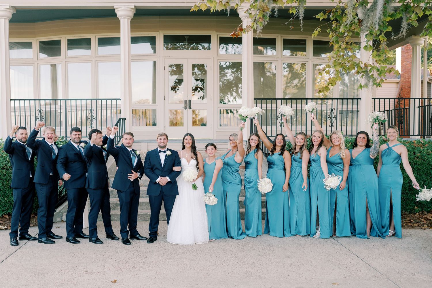 Large wedding party portrait with groomsmen in navy and bridesmaids in turquoise dresses.