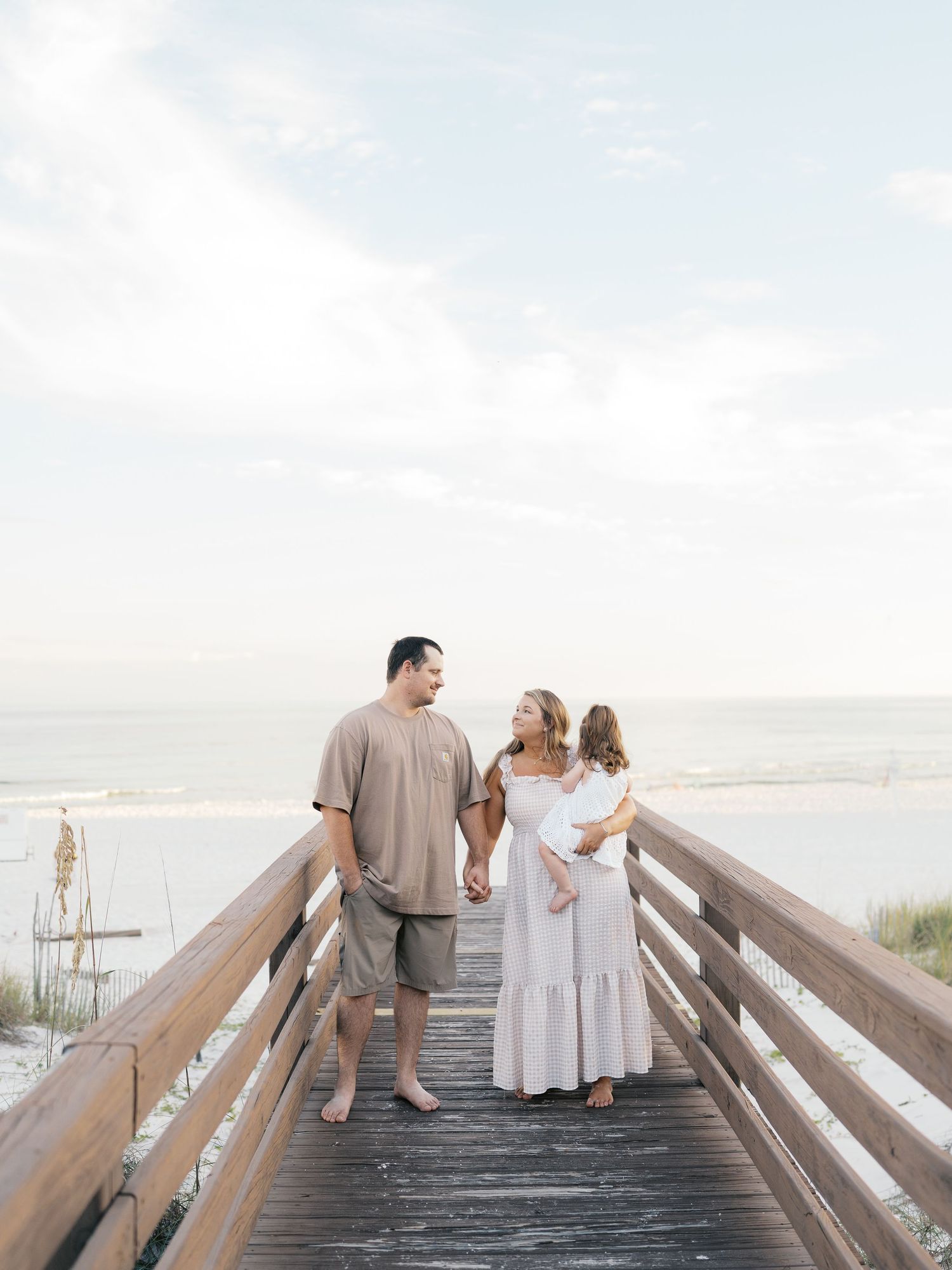 Family members hold hands while walking on a wooden beach boardwalk at sunset.