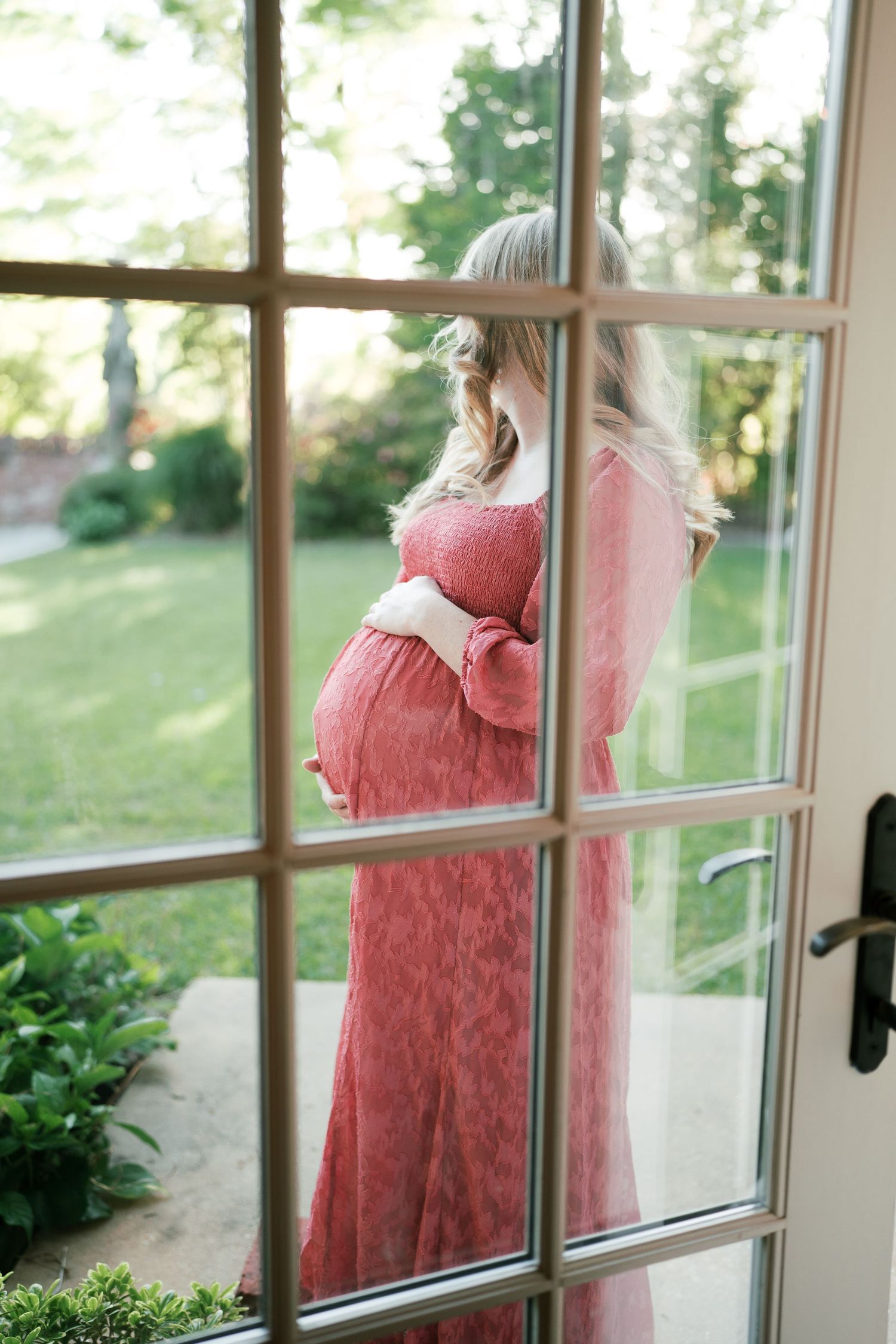 A pink dress is viewed through vintage windowpanes with garden scenery in the background.