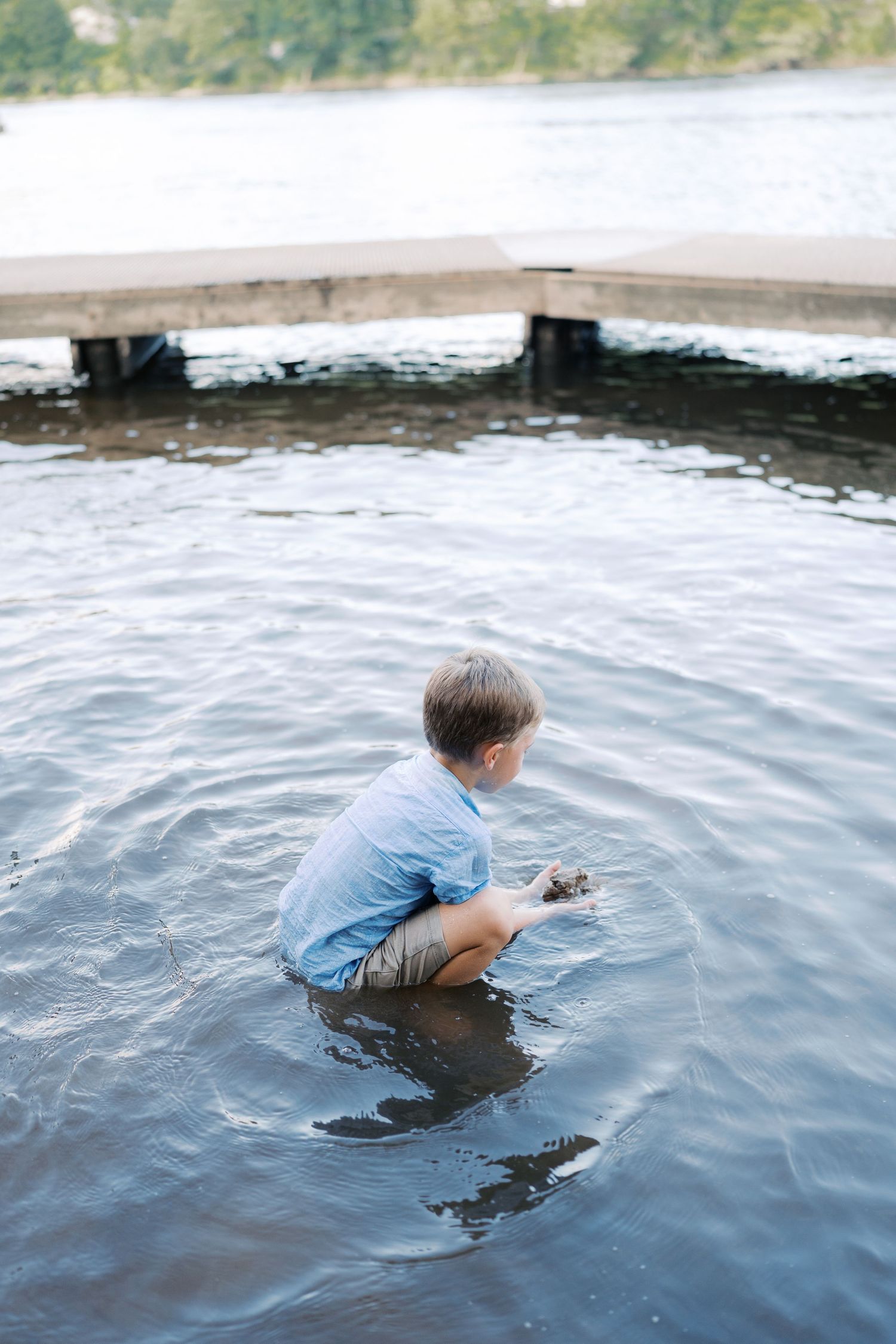 A child in blue clothing slides into lake water from a wooden dock.