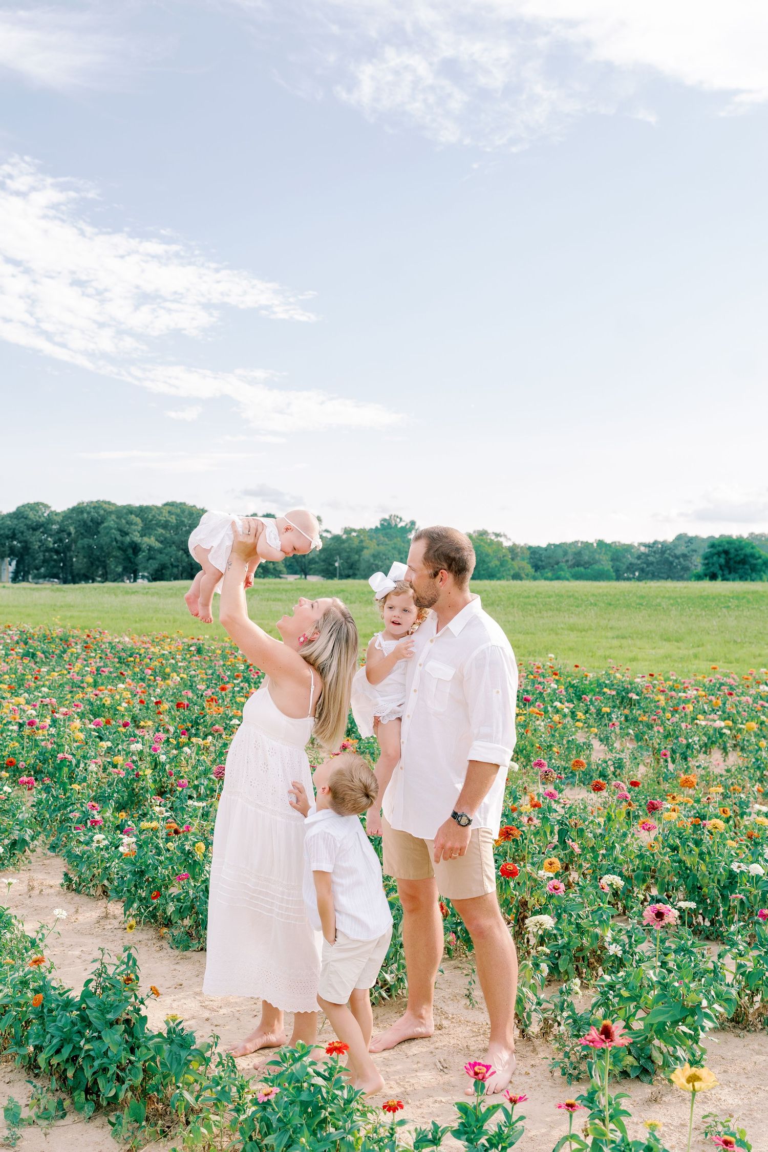 Family plays and laughs together in field of blooming flowers during summer photo session.