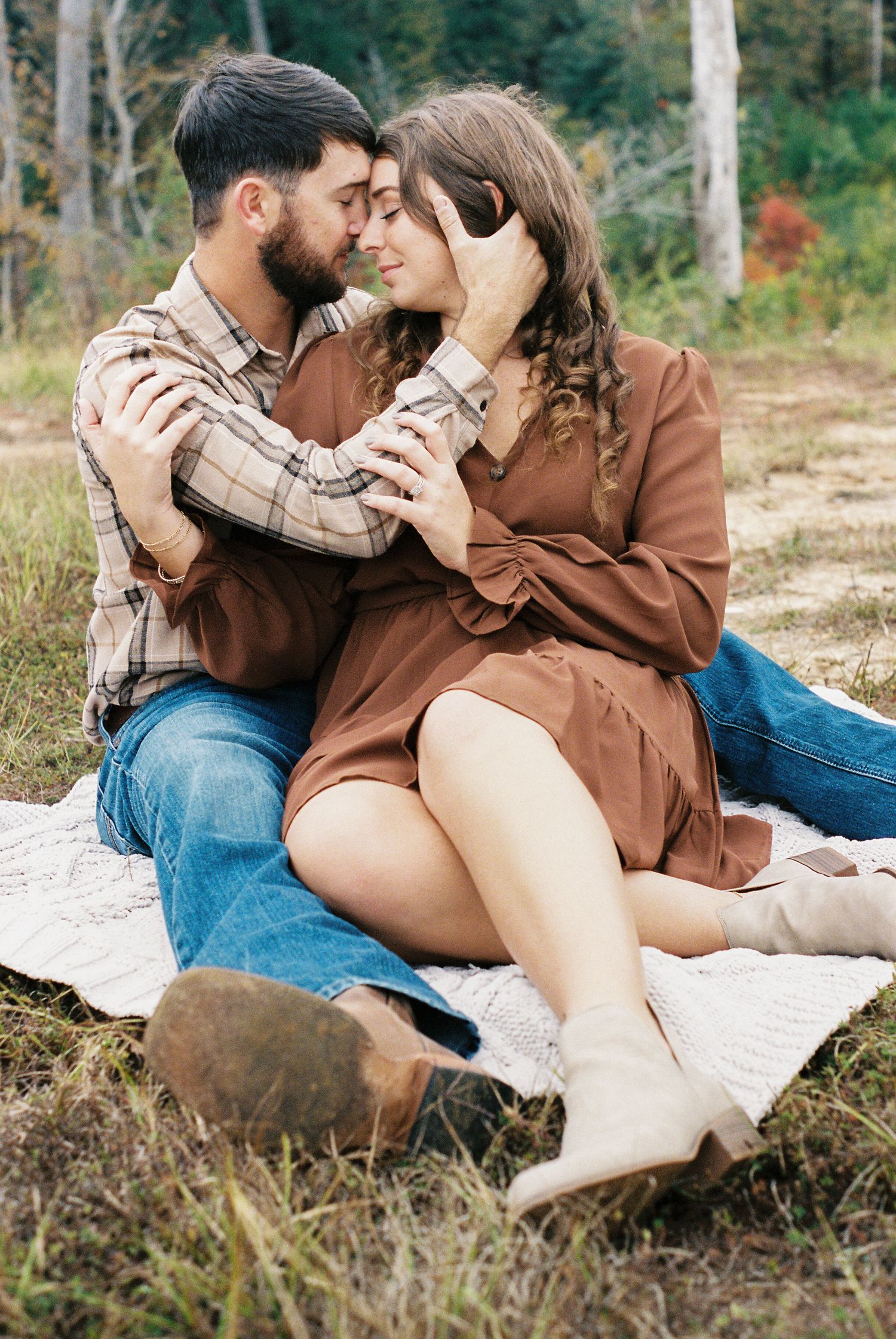 Romantic couple embracing on blanket in natural outdoor setting.