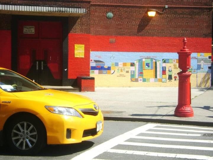 Yellow taxi cab parked along red brick building on city street.