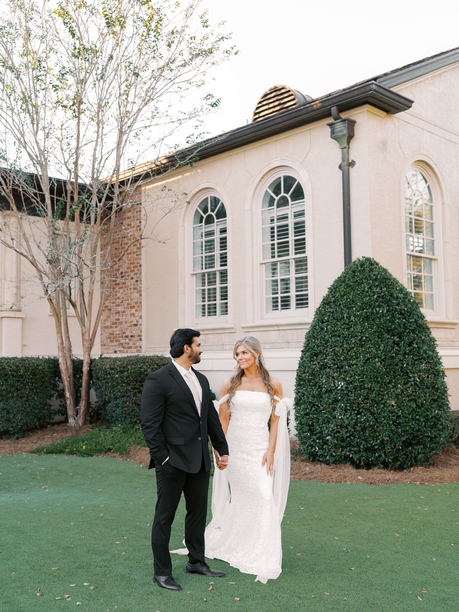 Elegant couple poses on manicured lawn in front of classic architecture.