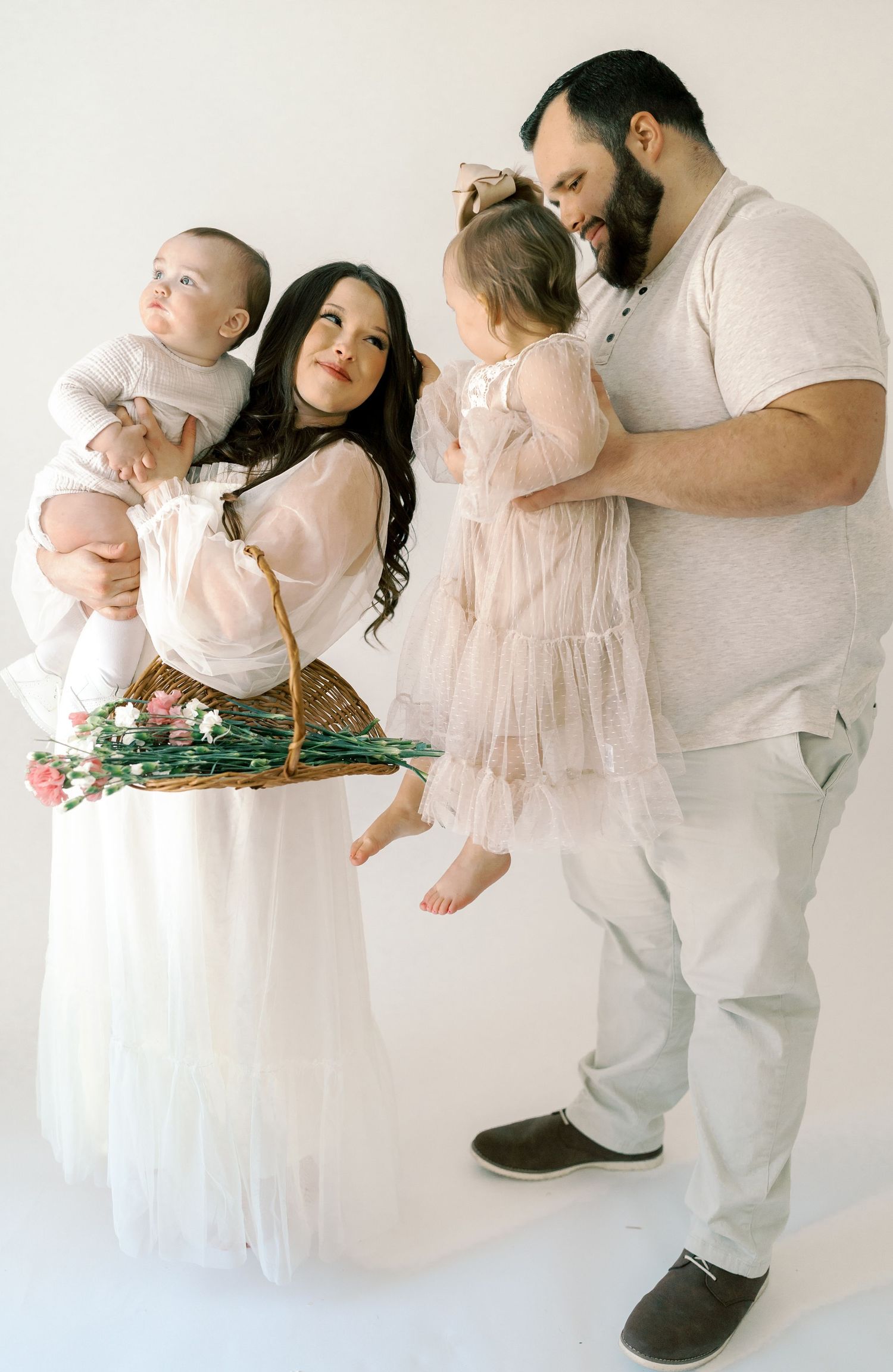 Family portrait in soft white clothing against a minimalist backdrop with floral accents.