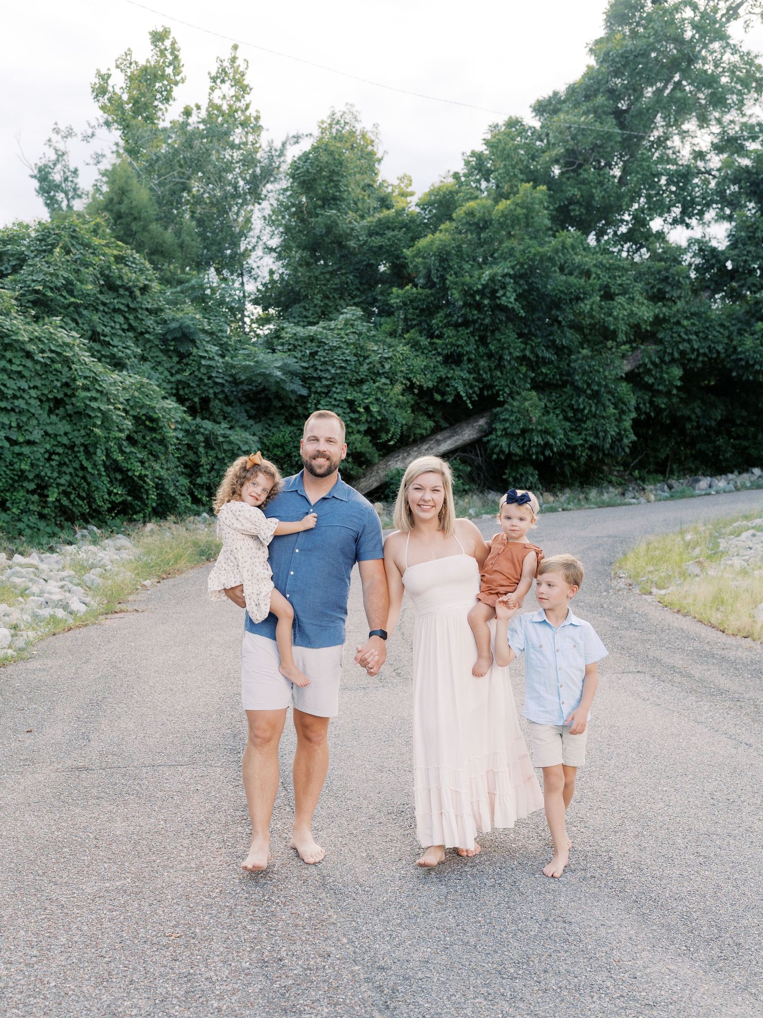 A family of five walks together on a gravel path surrounded by green trees.