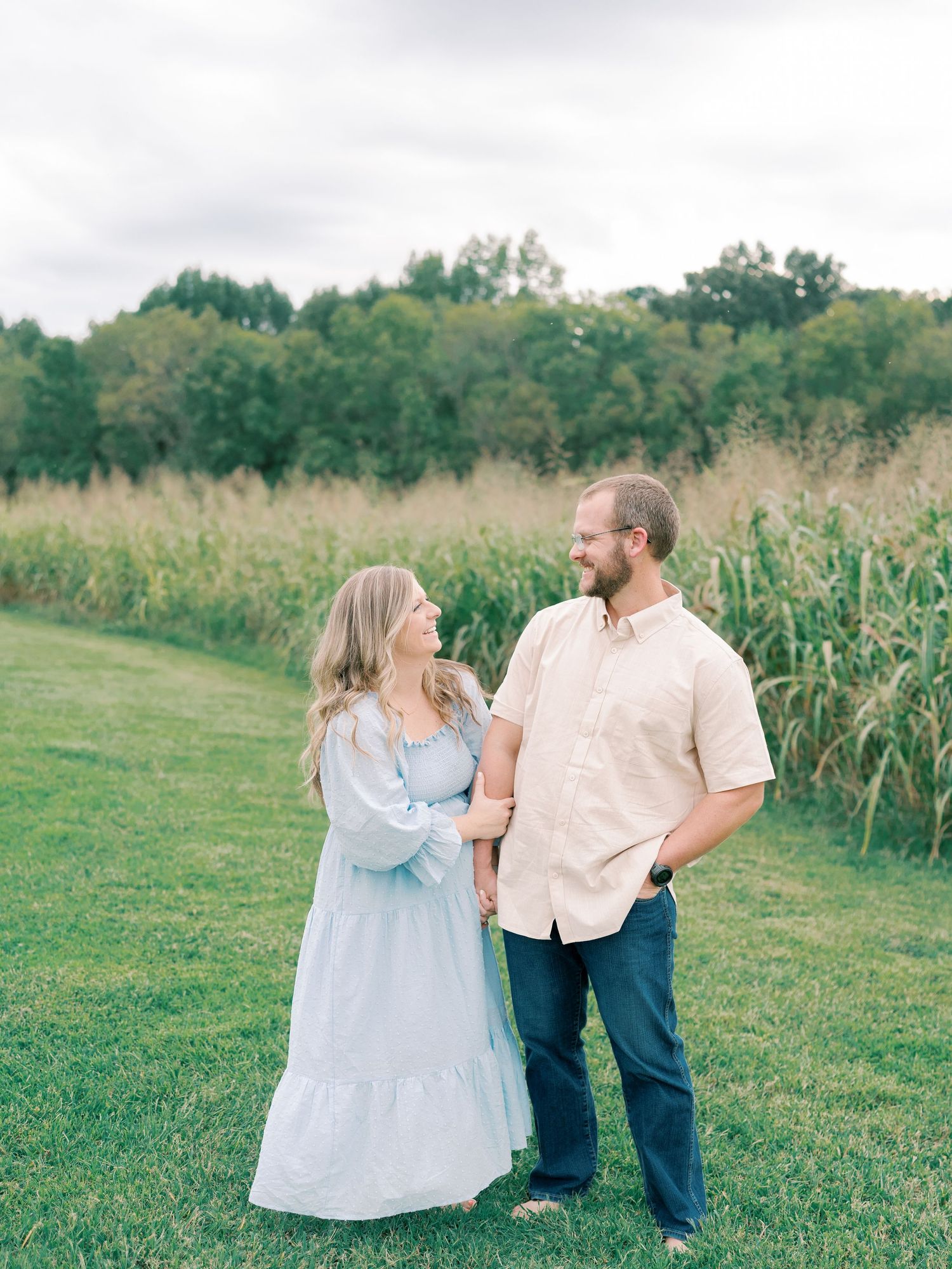 Family portrait in soft blue and white outfits against green summer field.