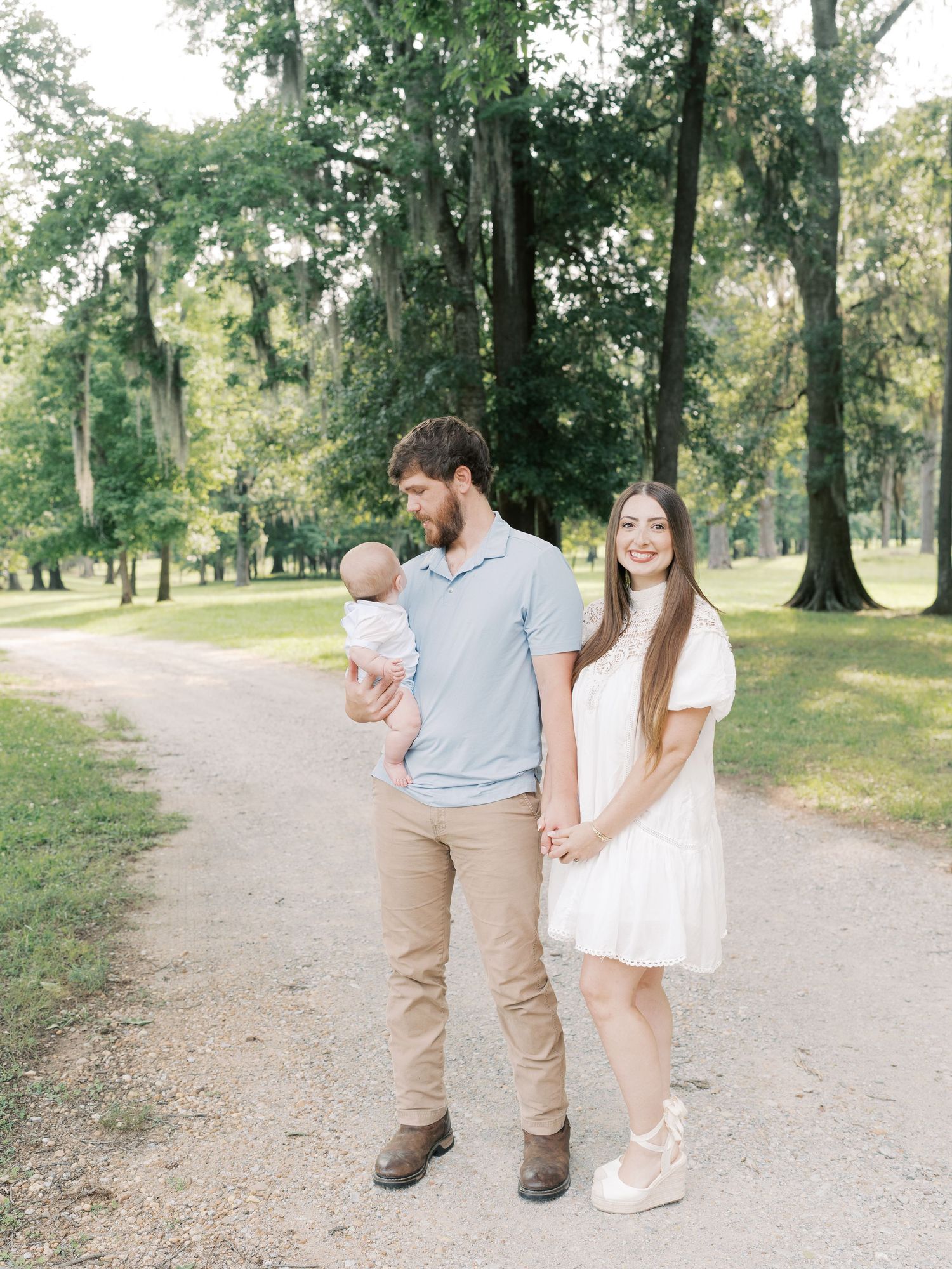 A family enjoys a casual stroll together on a winding park trail among tall trees.