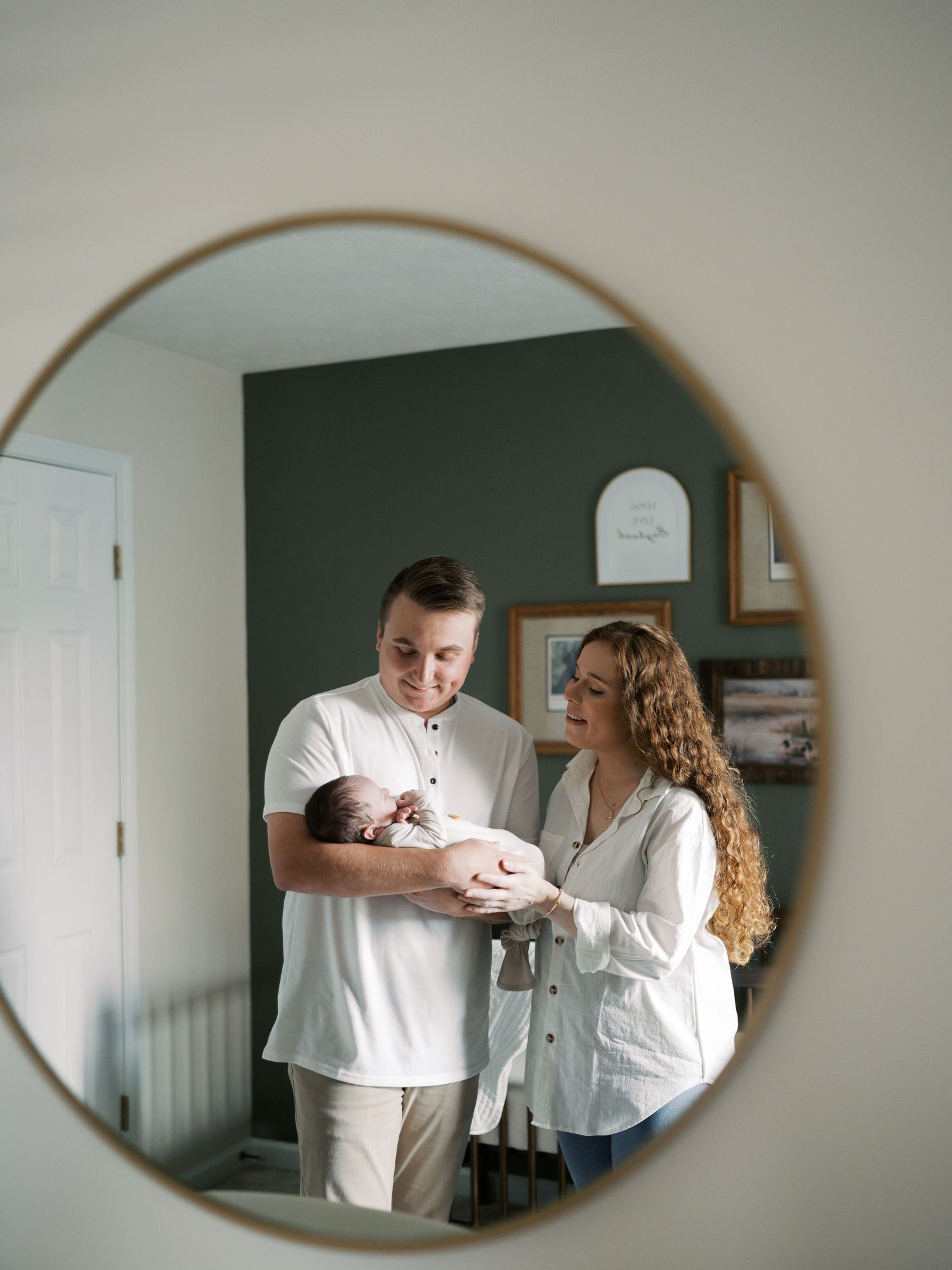 Mirror reflections capture sweet family moments in a nursery with sage green walls.