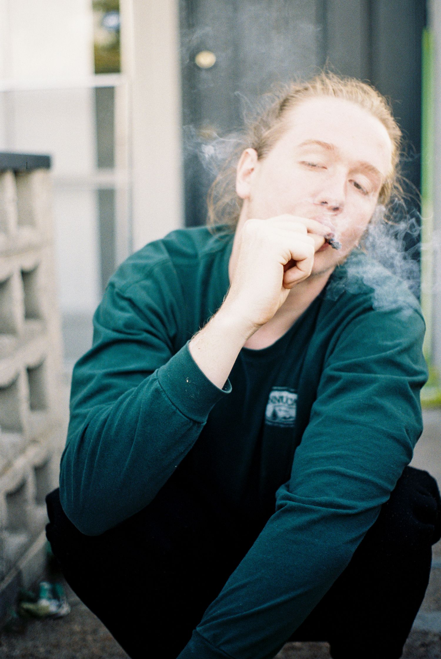 Person in green sweatshirt smoking while sitting outdoors.