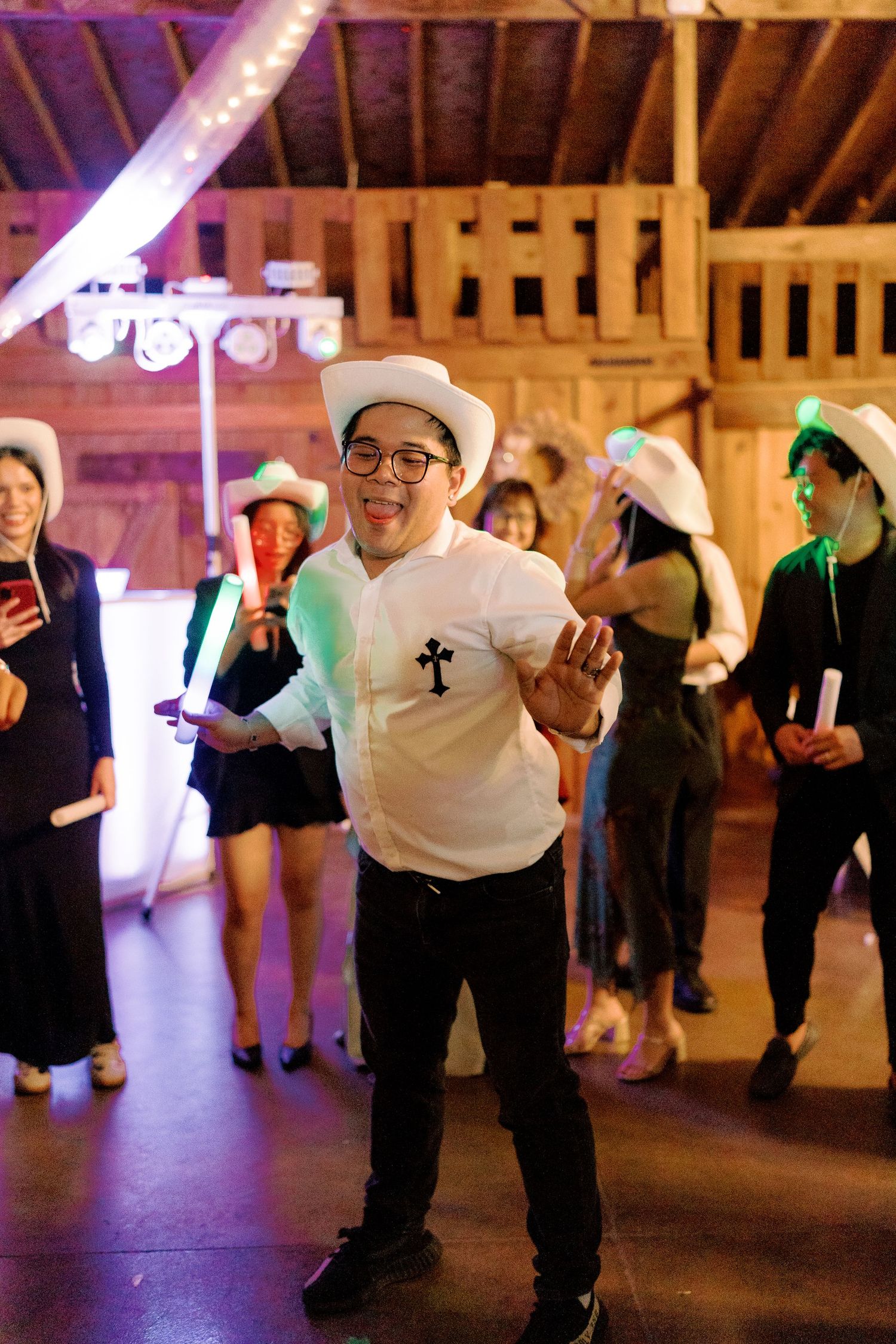 Dancers in white shirts and cowboy hats performing synchronized moves in a barn setting.