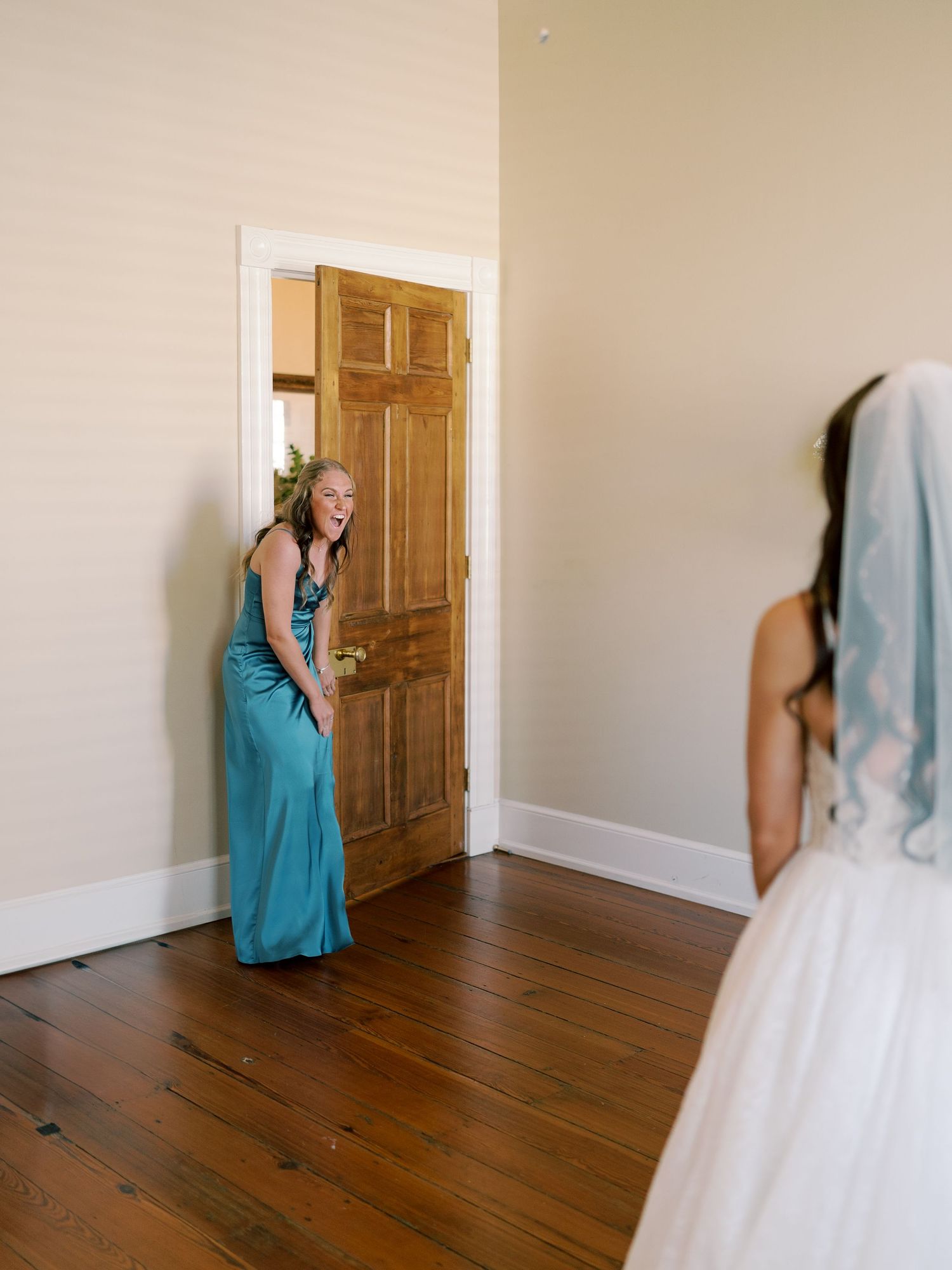 First look moment captured in a bright room with hardwood floors and wooden door.