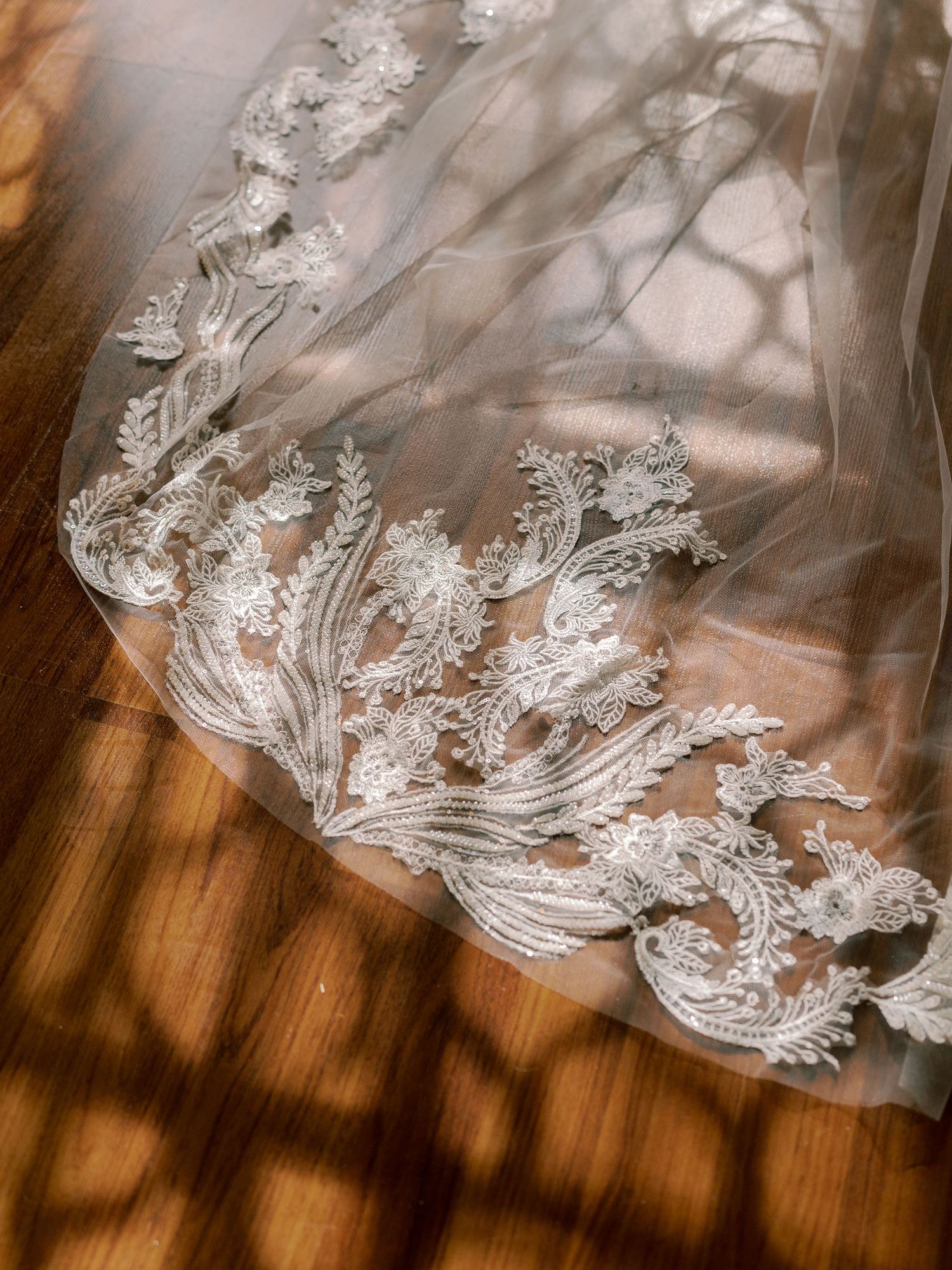 Detailed shot of intricate lace pattern on wedding veil hem with sunlit shadows.