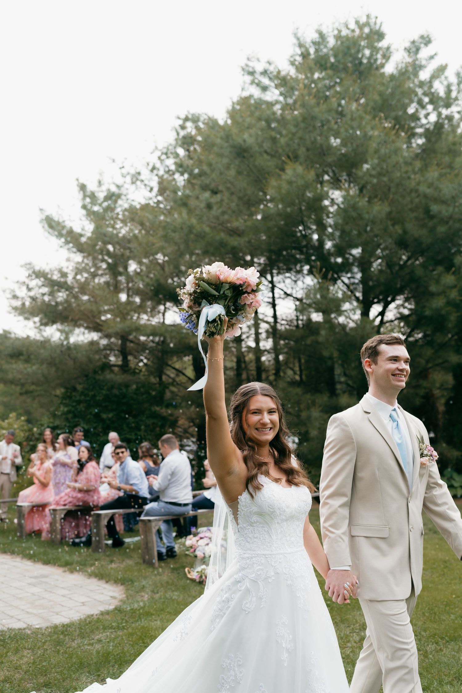 A celebratory moment as newlyweds walk past guests seated on outdoor benches.