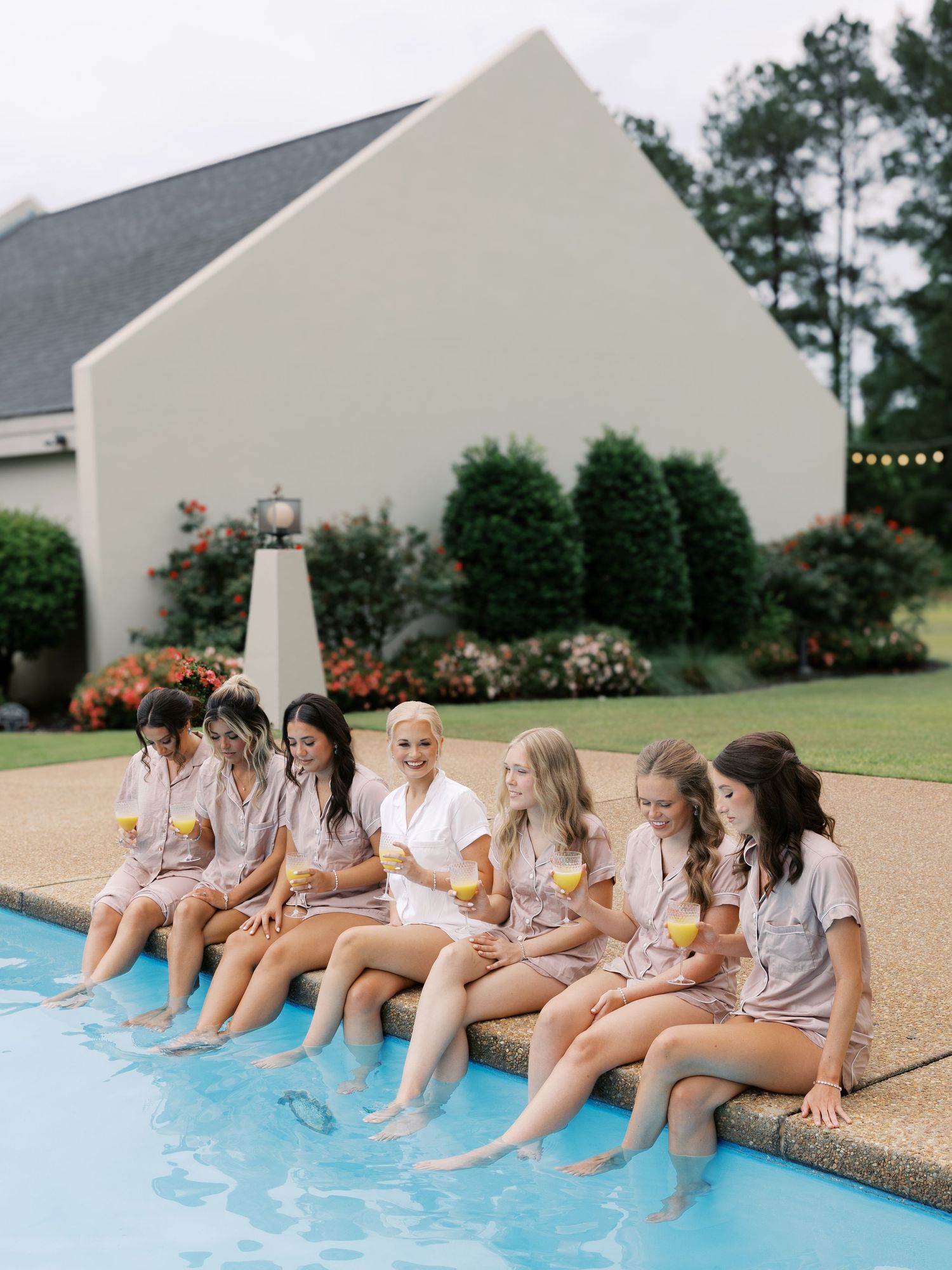 Group sitting at poolside with feet in water wearing casual attire.