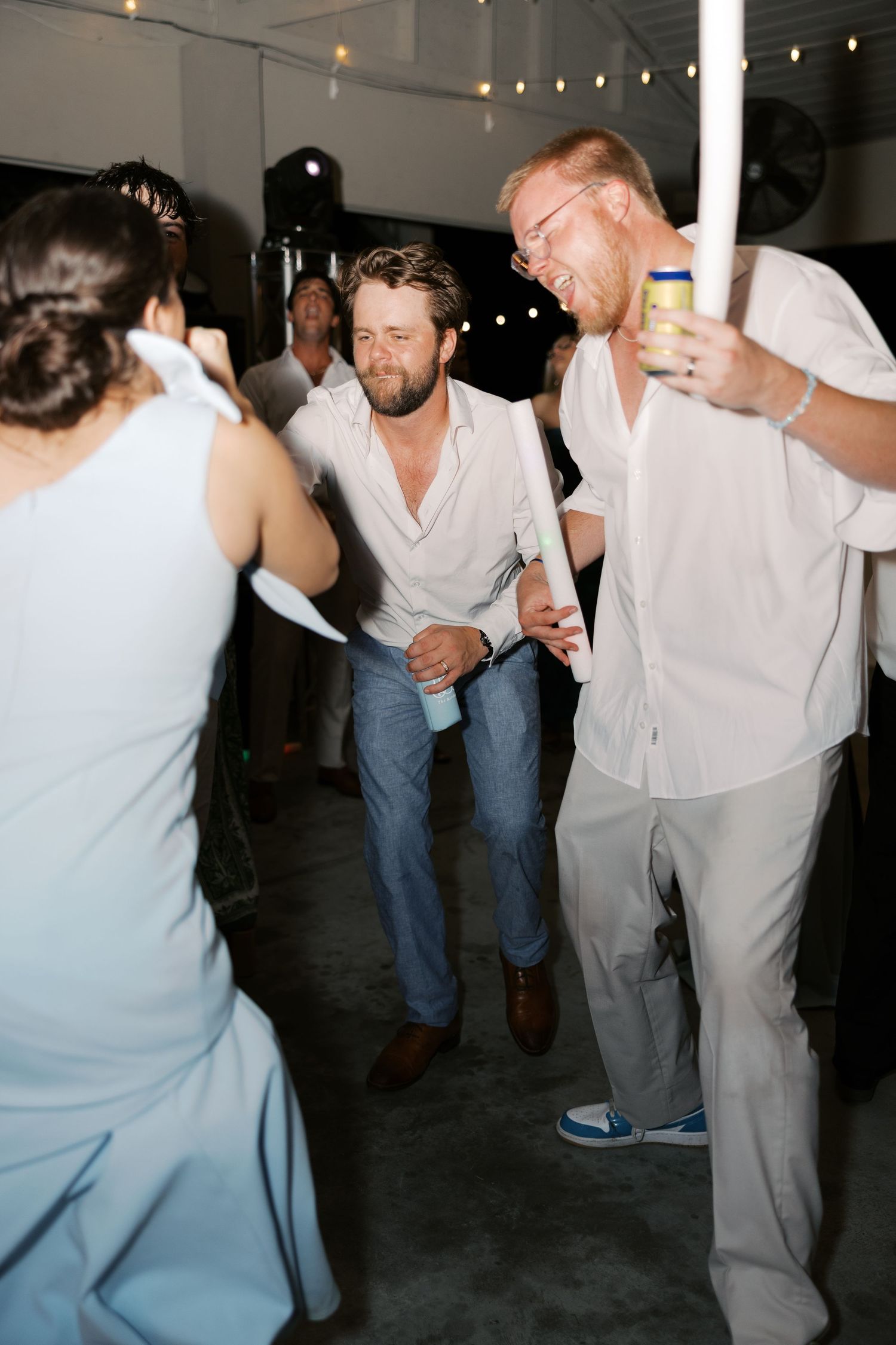 Lively dance floor scene at a wedding reception with guests in light colored attire.