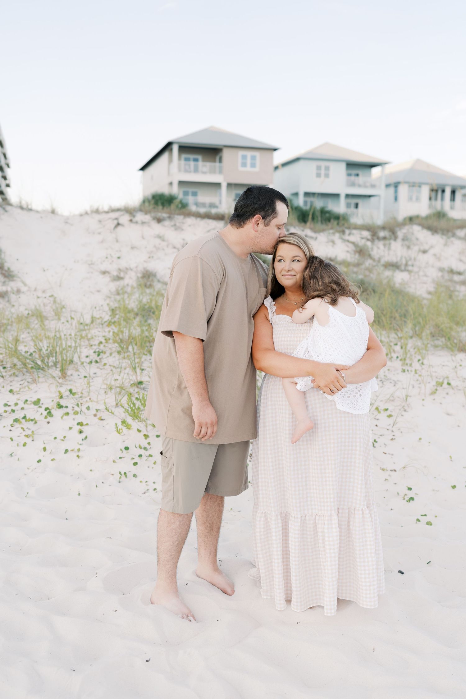 Sweet family interaction during beach photography session with coastal architecture visible.