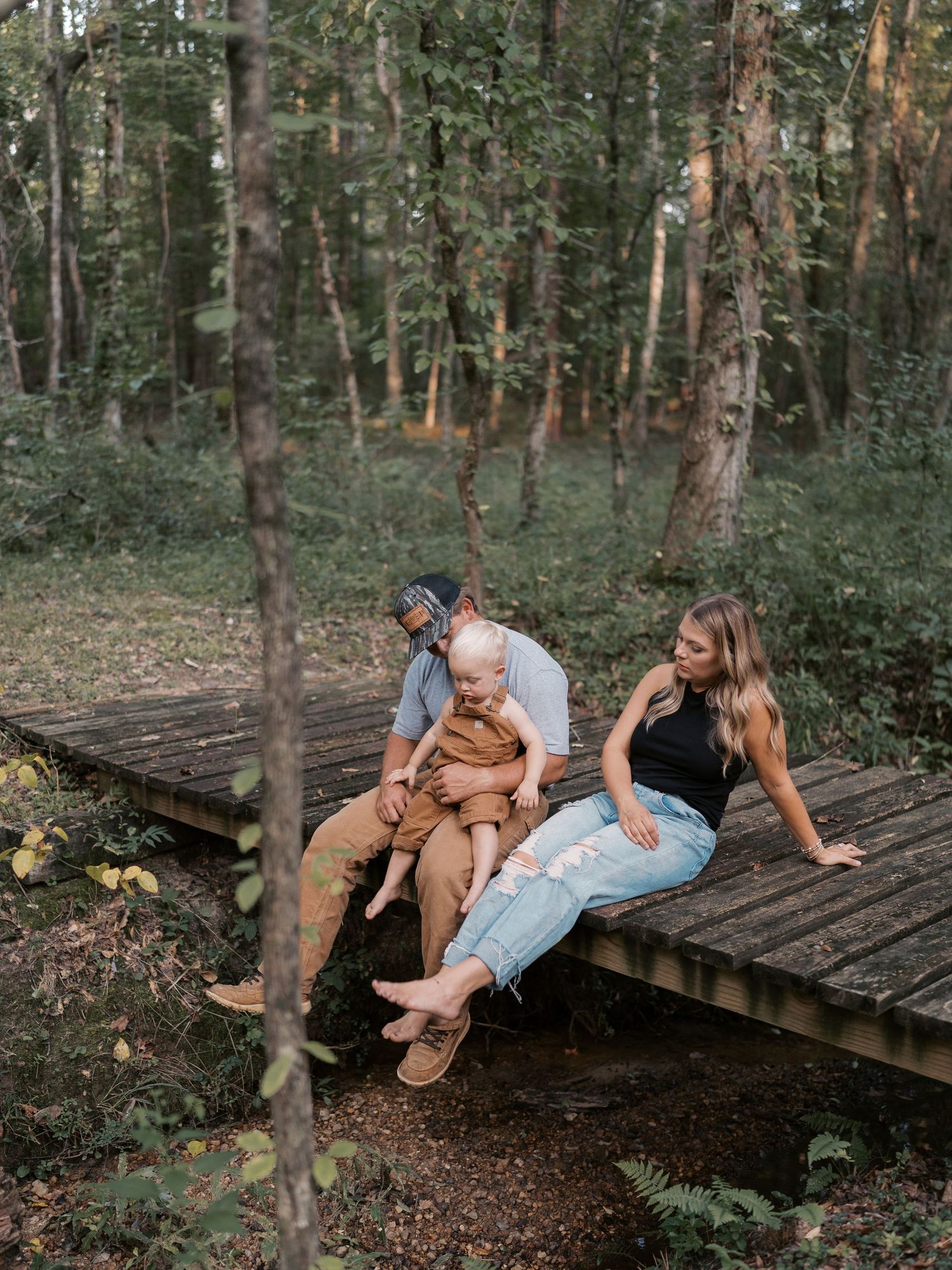 A family shares tender moments together on a wooden bridge in a forest setting.