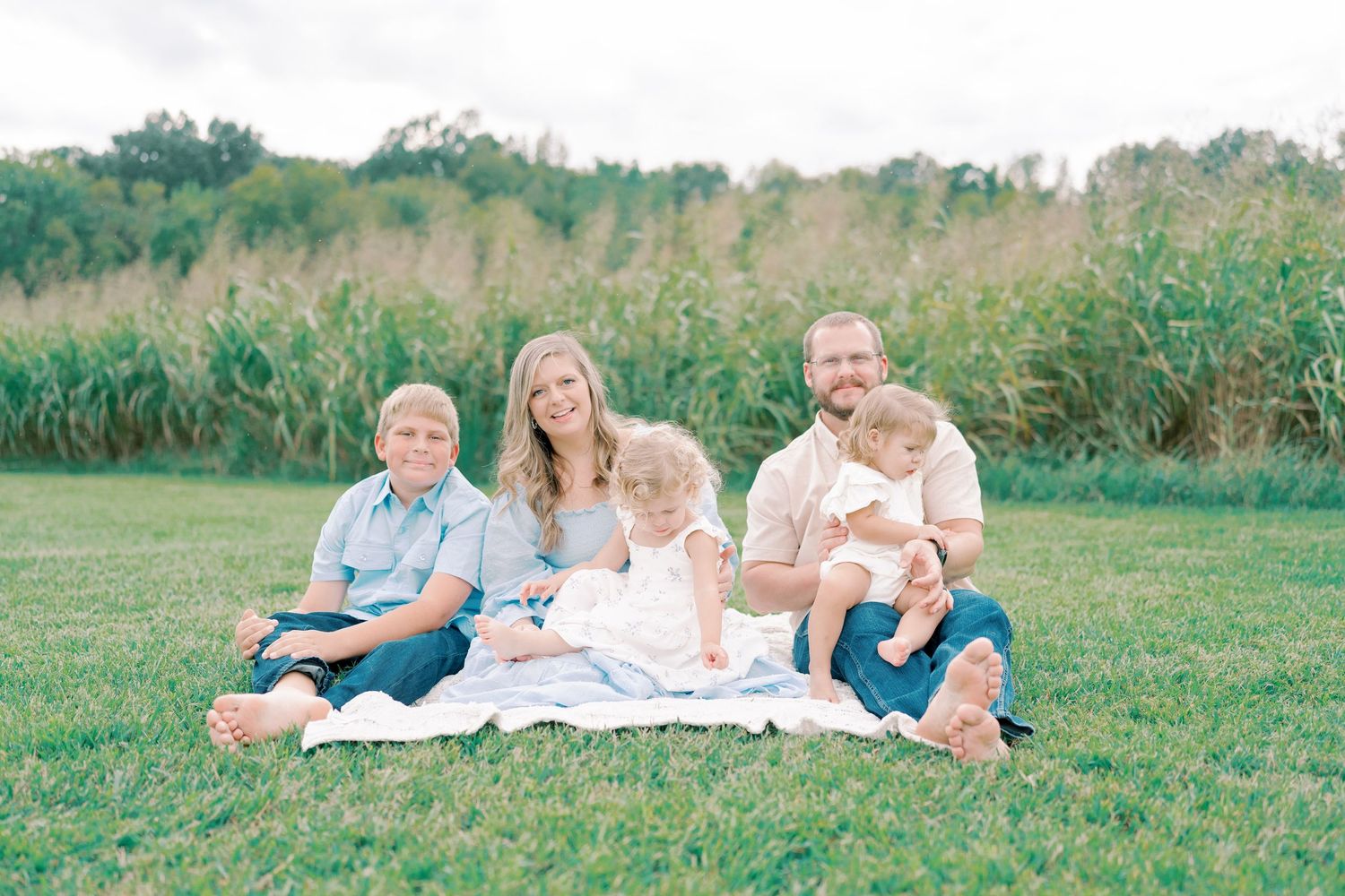 Family relaxes together on blankets in a sunny field during an outdoor photo session.