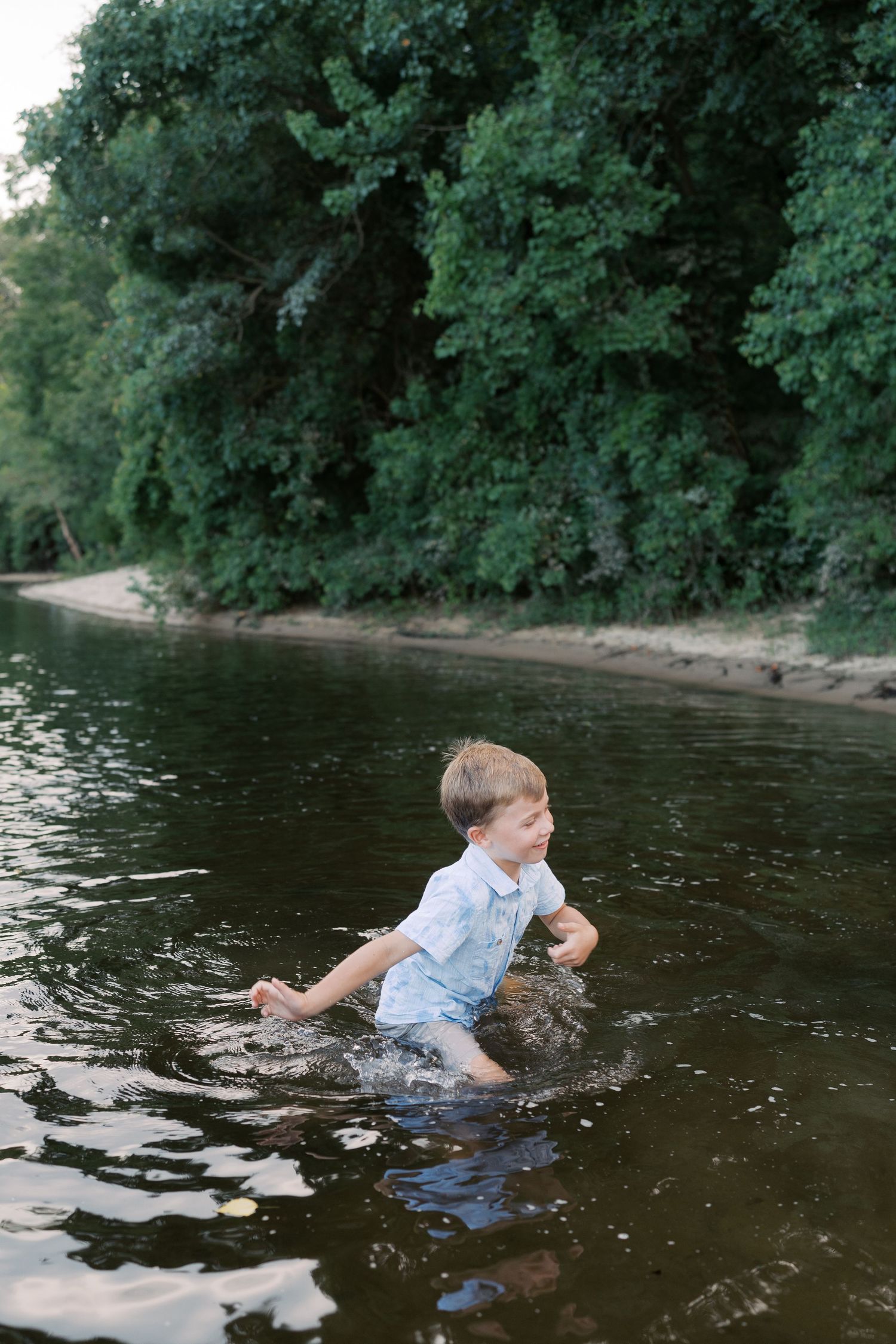 Child playing and making splashes in a river surrounded by lush greenery.