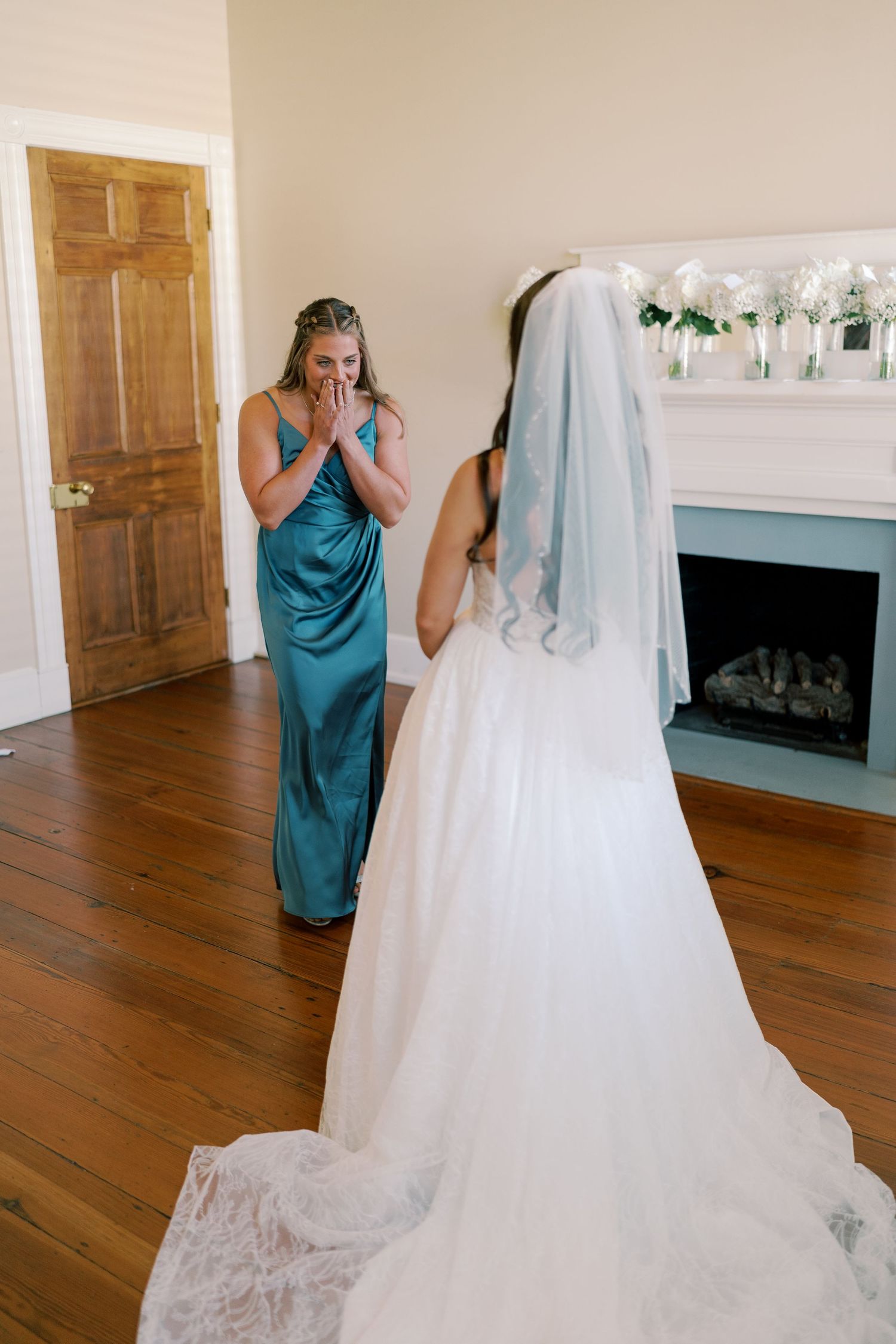 Emotional first look reaction between bridesmaid and bride in an elegant room with fireplace.