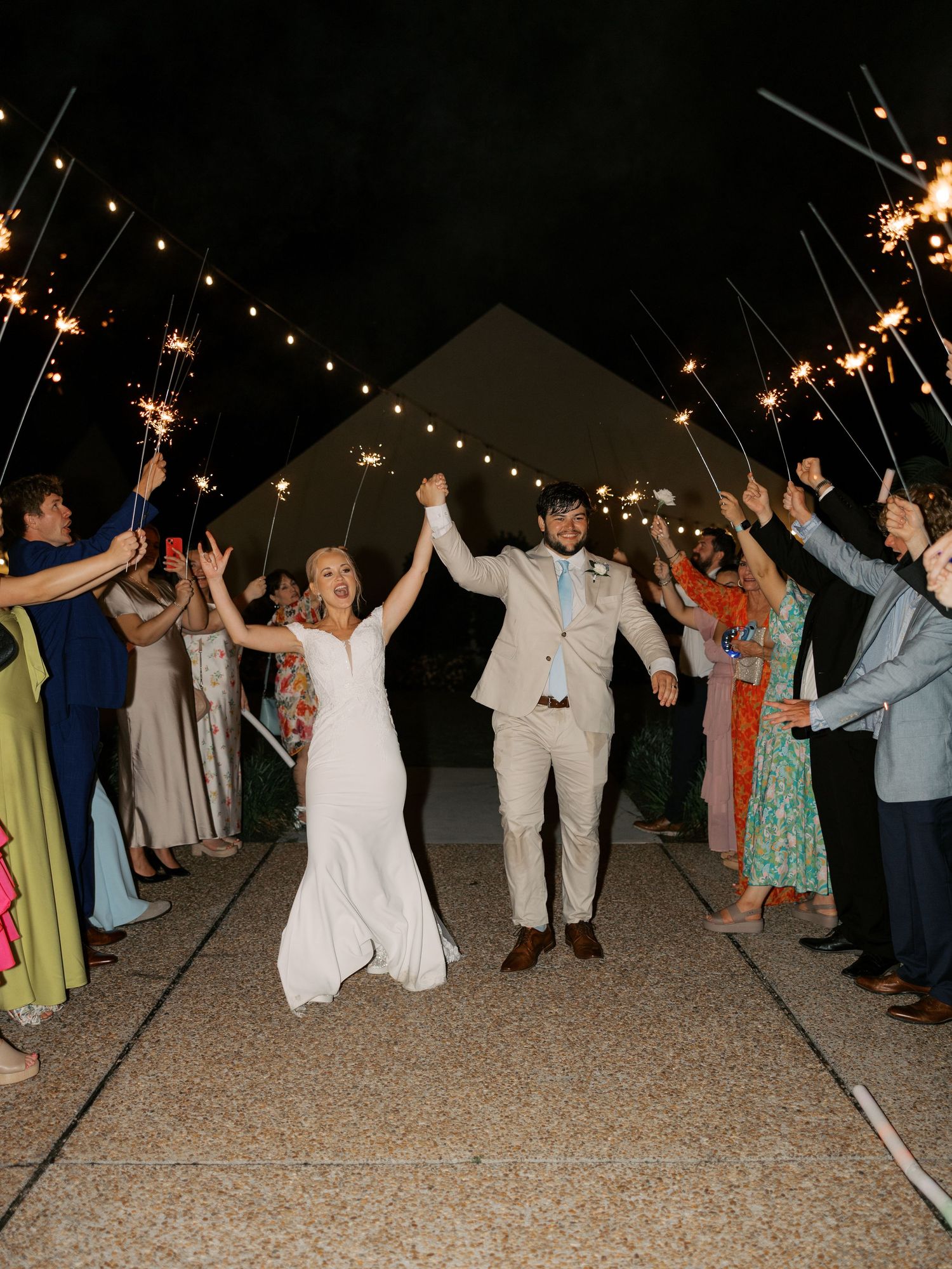 Wedding guests holding sparklers form a tunnel during the newlyweds' exit celebration.