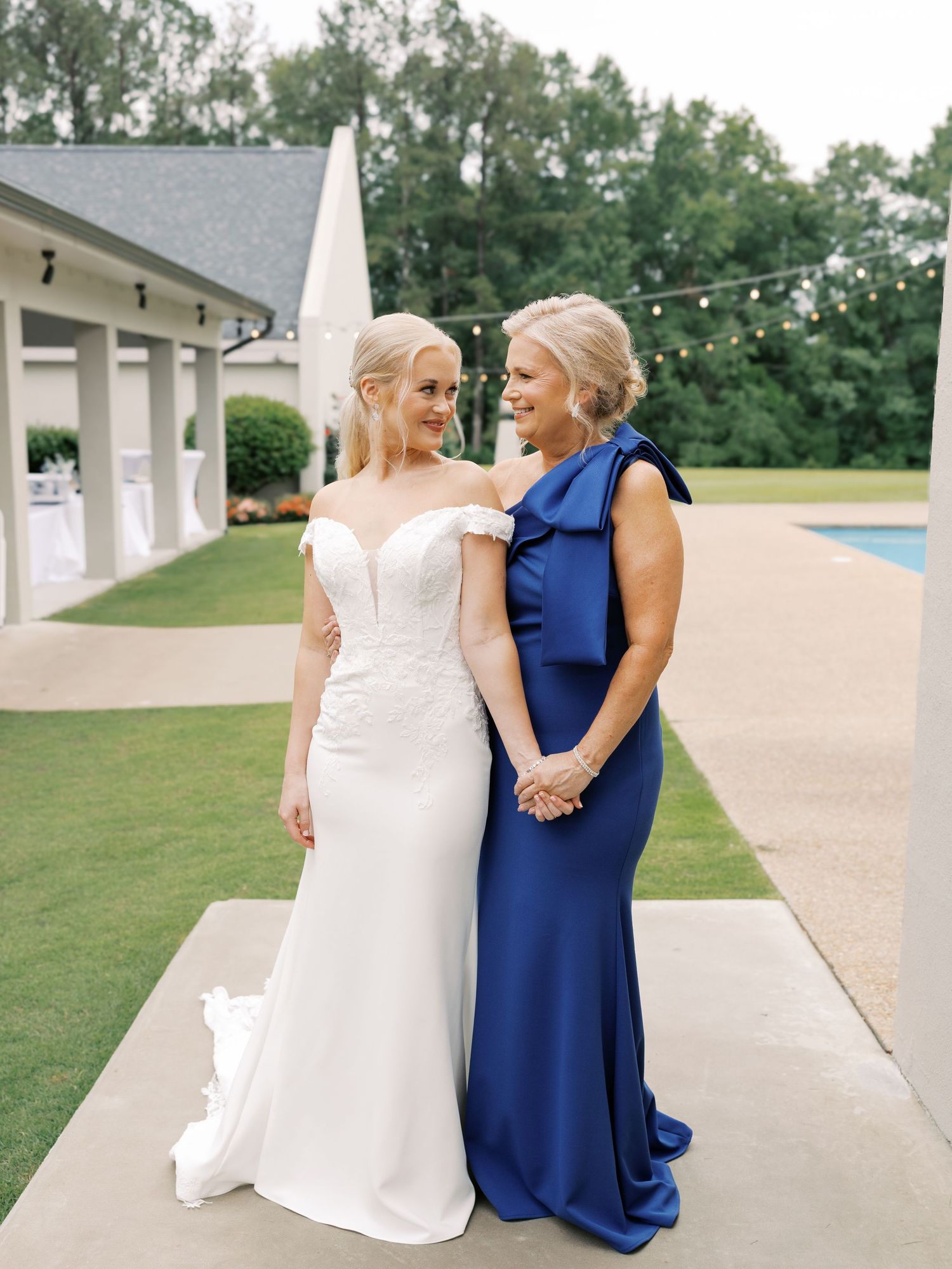 A bride in white and woman in navy share a sweet moment together in a series of outdoor wedding photos.