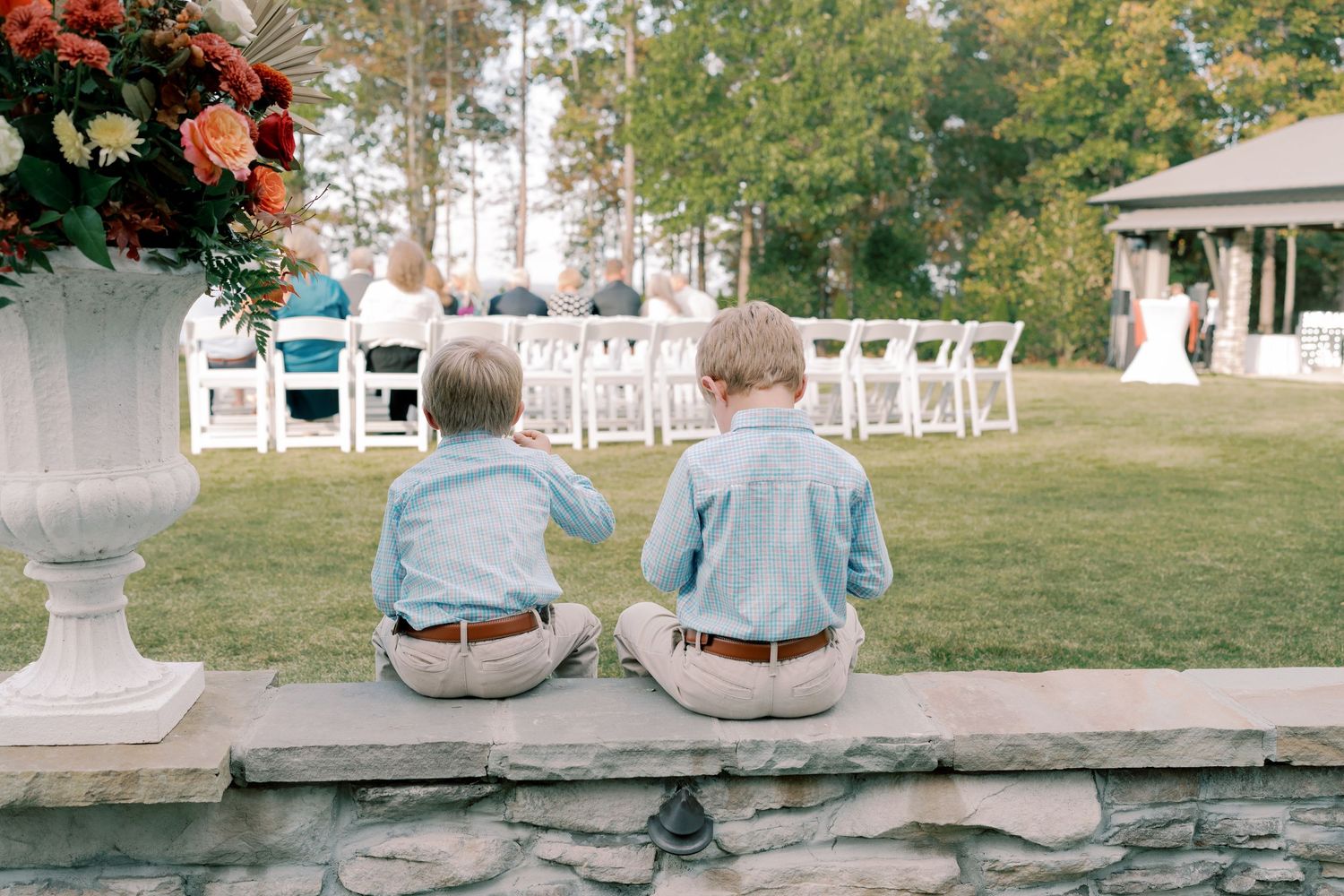 Wedding guests sitting on stone wall during outdoor reception.
