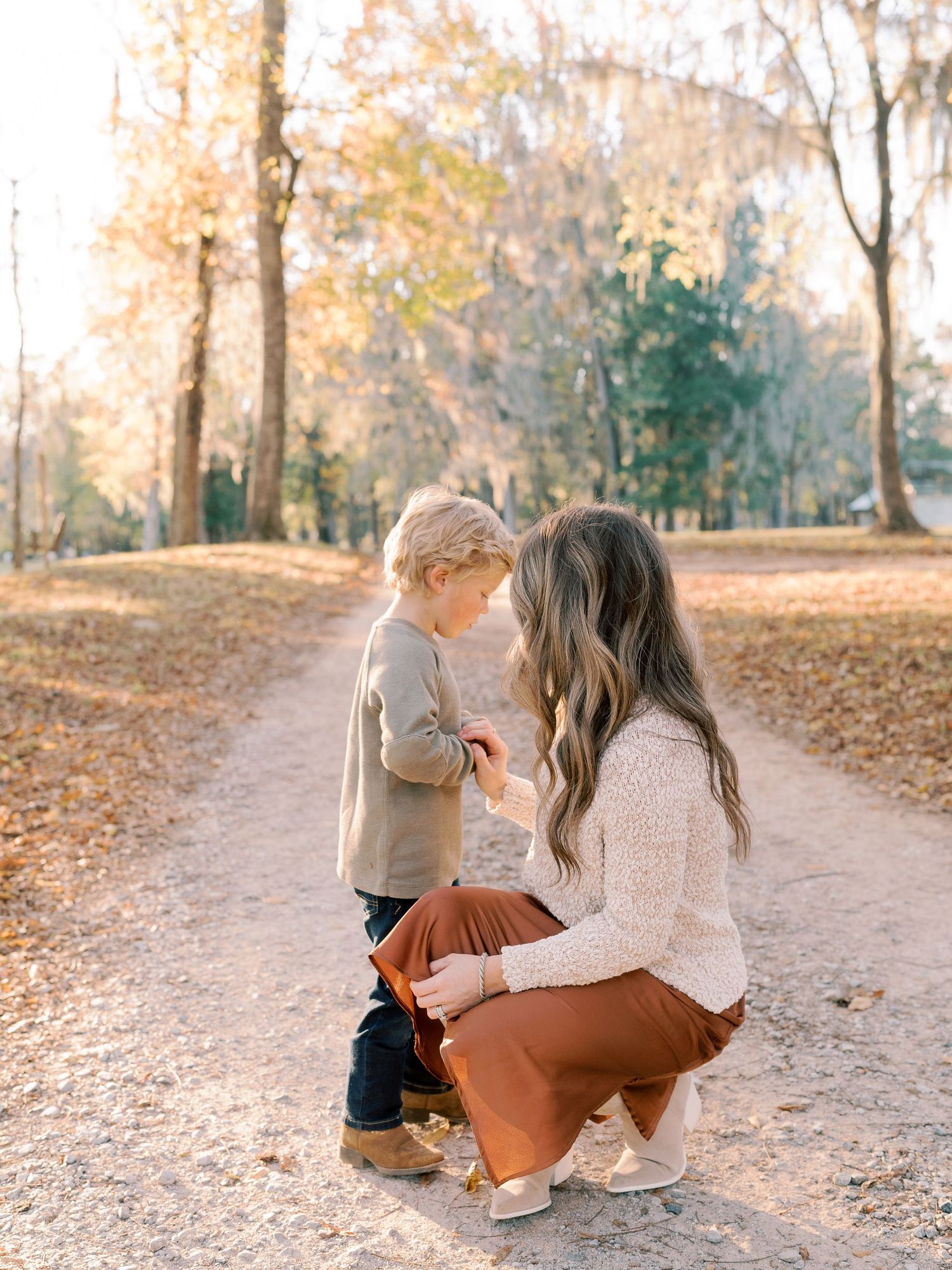 Intimate moment between parent and child on dirt path surrounded by fall foliage.