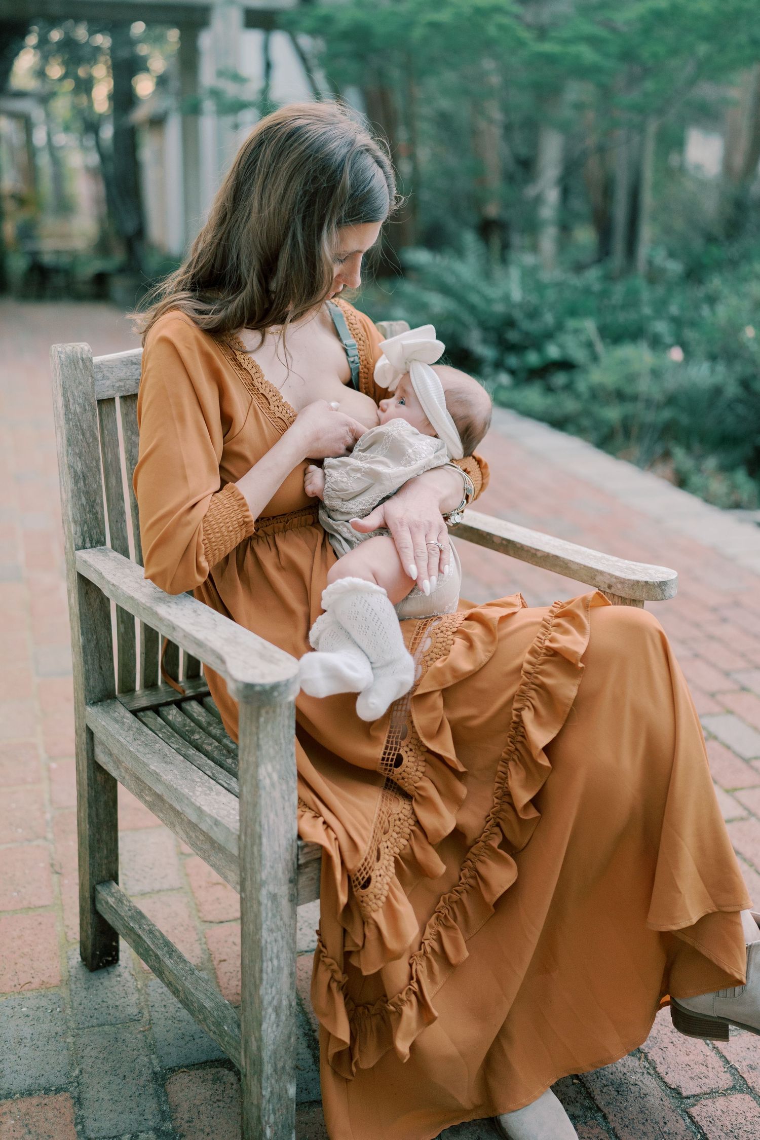 A caramel-colored ruffle dress flows elegantly while seated on a wooden bench in a garden setting.