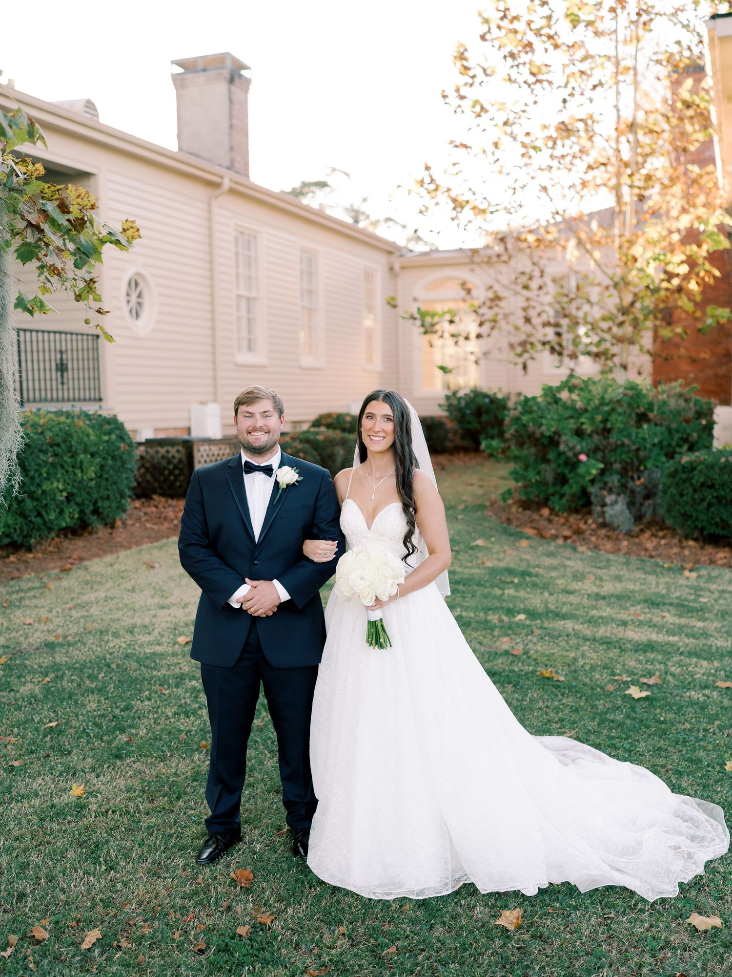 Wedding couple poses in front of classic white building during autumn.